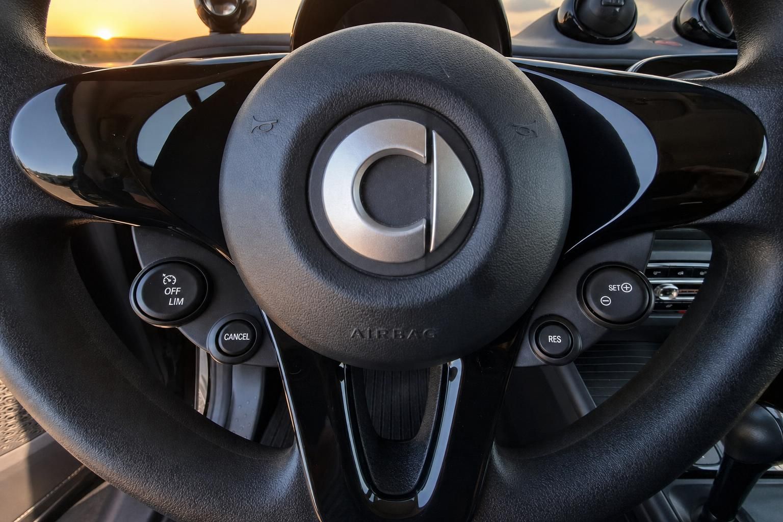 Lenkrad mit Tempomat-Bedienung im Smart Fahrzeug, Sonnenuntergang im Hintergrund