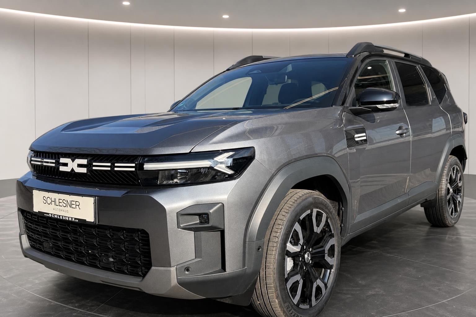 Dacia SUV grau Seitenansicht schraeg vorne mit Dachreling