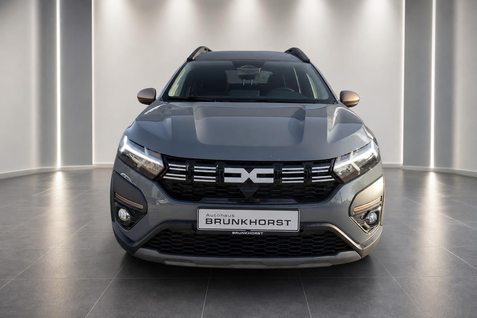 Dacia Frontansicht mit markanter Kühlergrill - graues SUV frontal im Autohaus-Showroom präsentiert