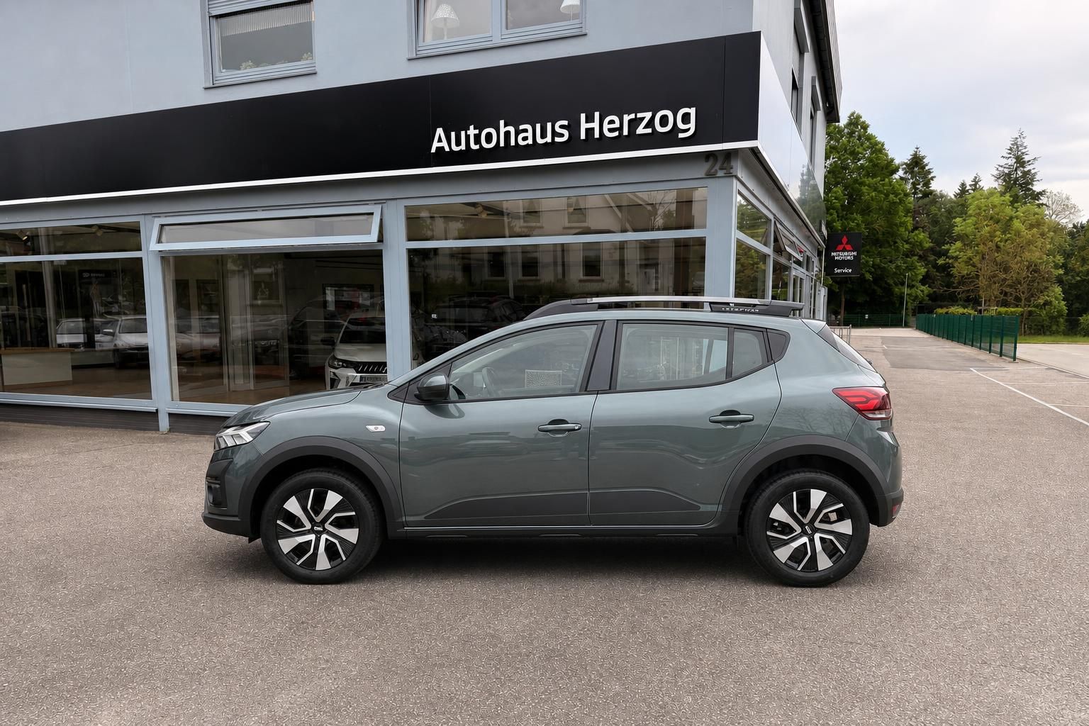 Dacia Sandero grün metallic Seitenansicht vor Autohaus Herzog Glasfront