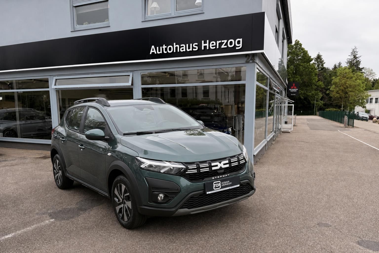 Dacia Stepway in Grau Schrägansicht vorne - SUV mit Dachreling und modernen Felgen vor Autohaus