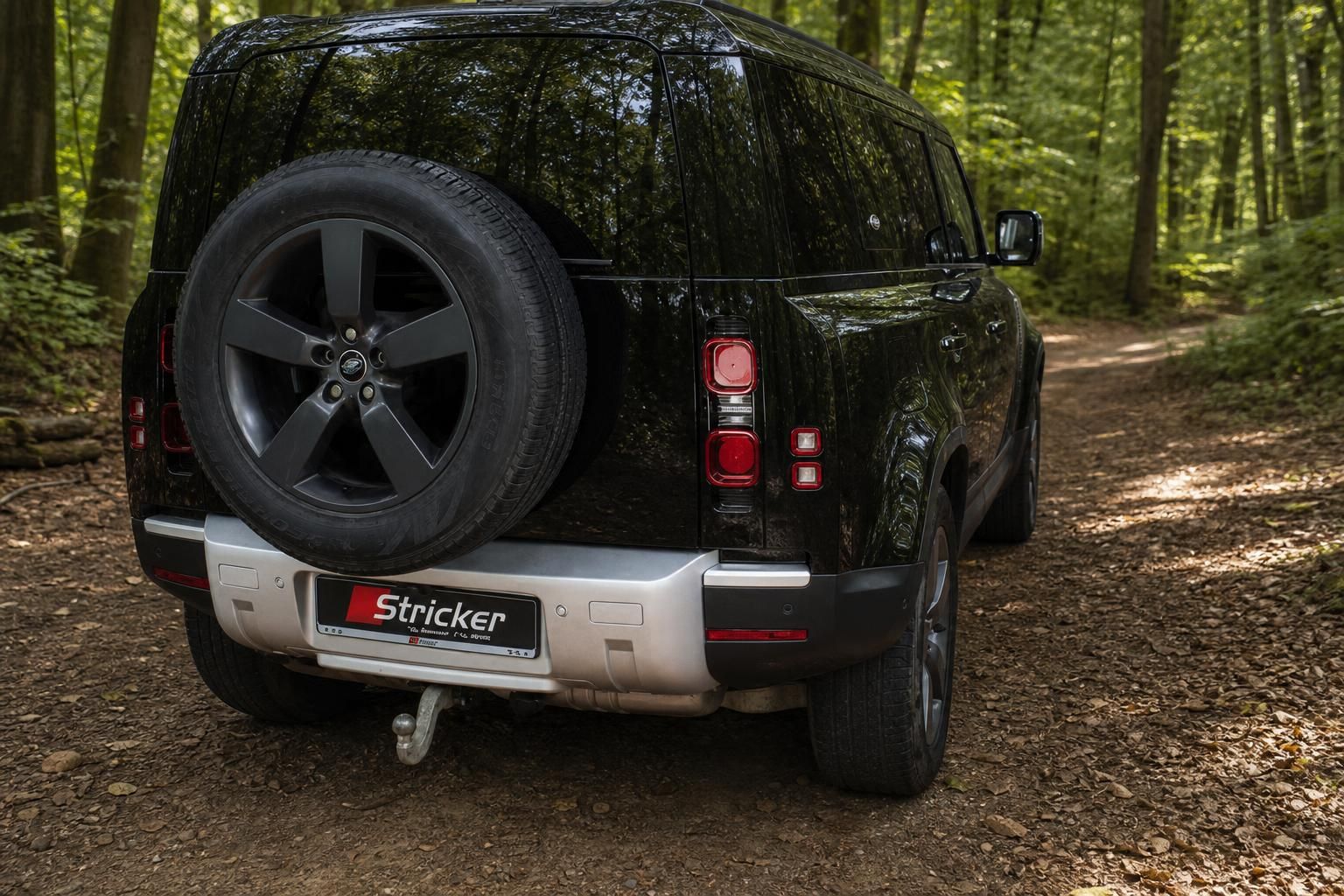 Land Rover Defender schwarz Heckansicht mit Reserverad im Waldweg