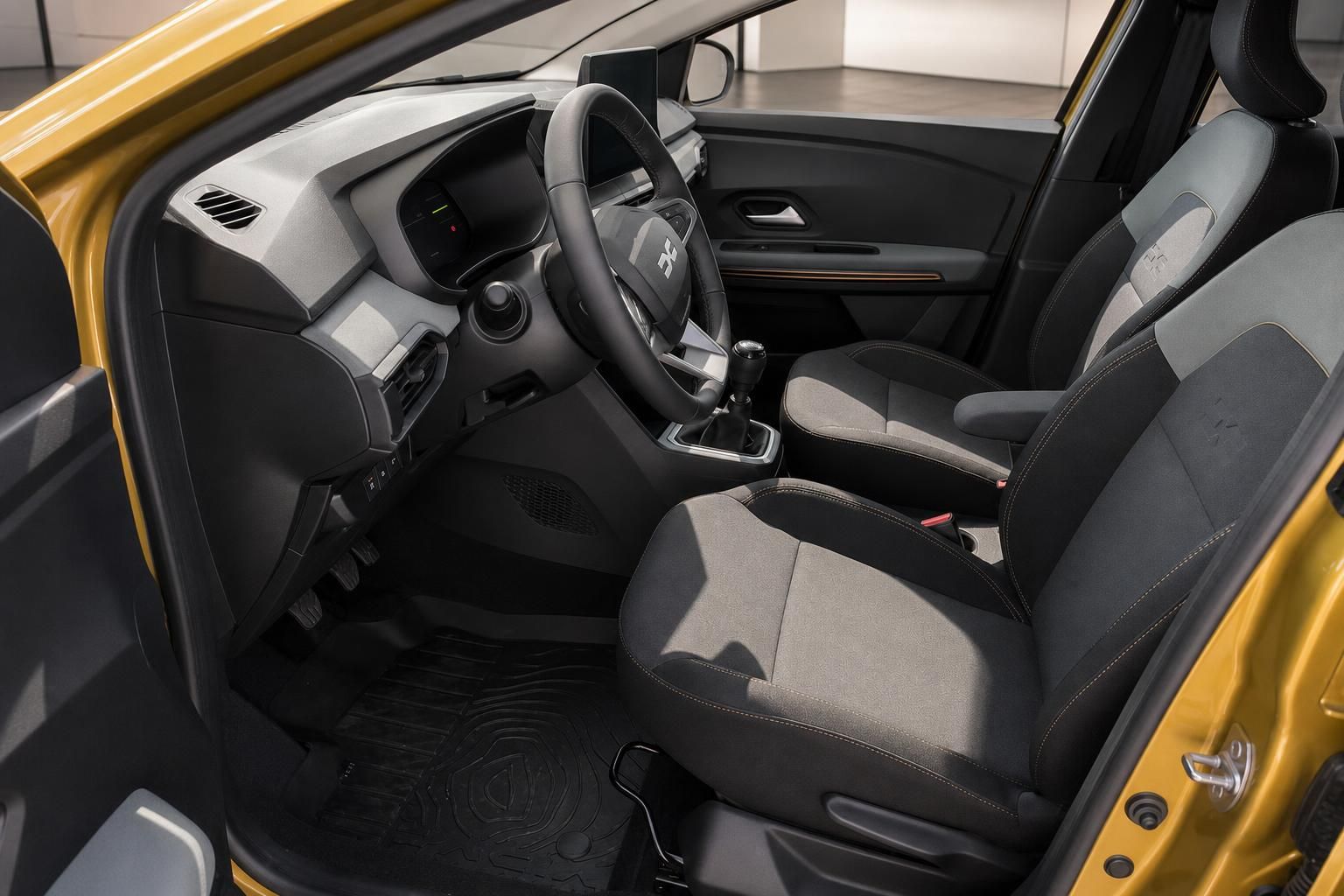 Dacia Innenraum Fahrerseite – Cockpit mit Lenkrad, Schaltknüppel und grauen Stoffsitzen in Gelb