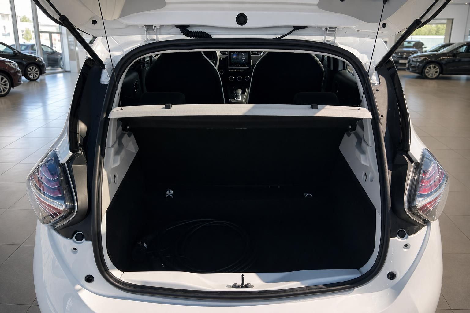 Geöffneter Kofferraum eines weißen Elektroautos mit schwarzer Innenausstattung im Autohaus-Showroom