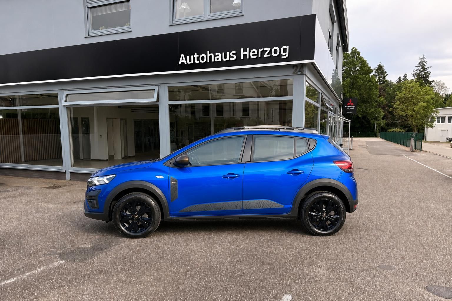 Blauer Dacia Stepway SUV Seitenansicht mit schwarzen Felgen vor Autohaus