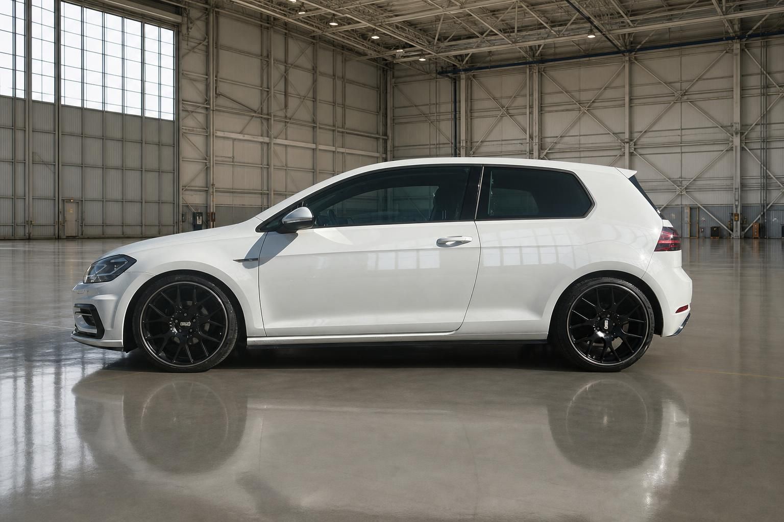 Weißer Volkswagen Golf Seitenansicht mit schwarzen Felgen in moderner Industriehalle