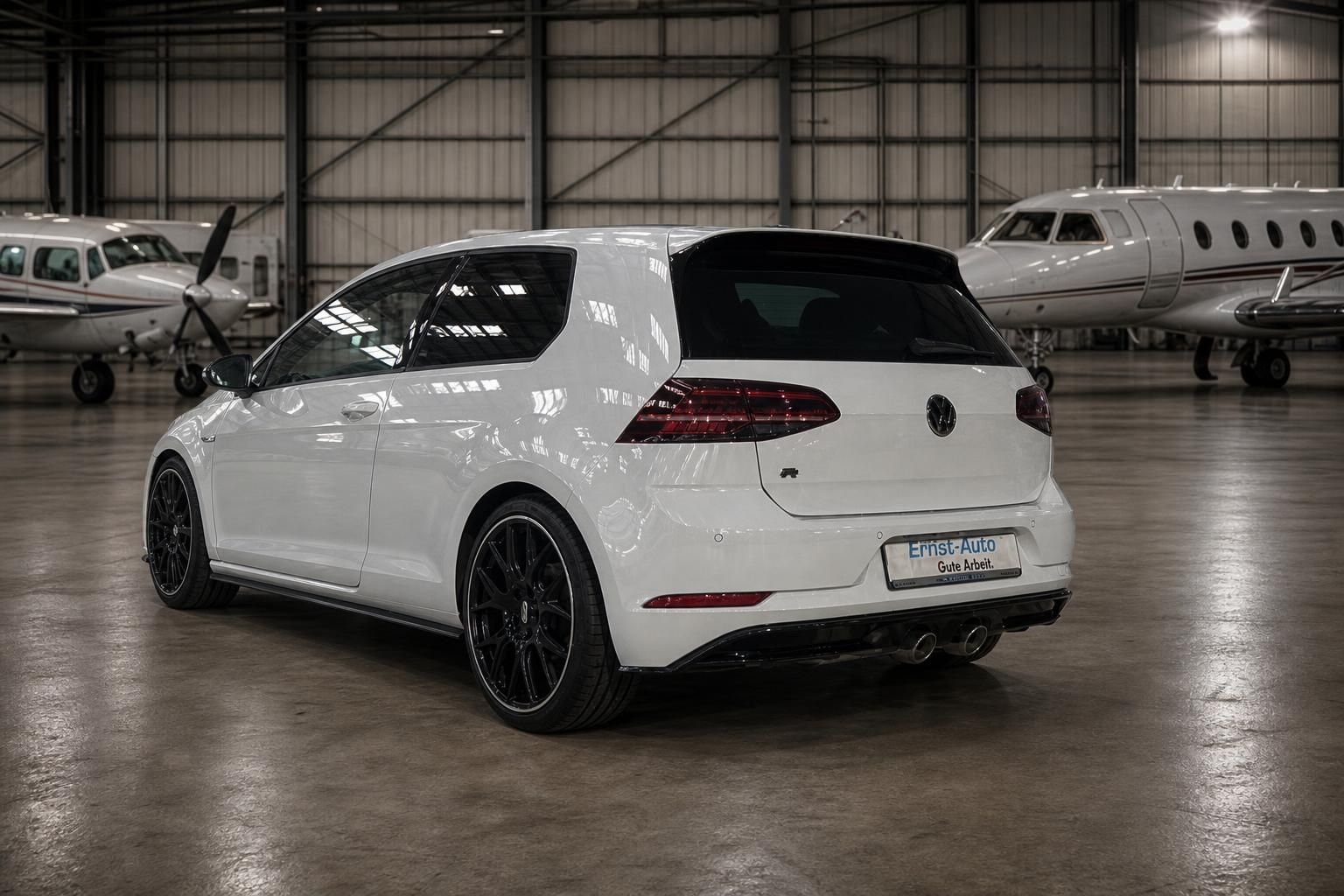 Weißer Volkswagen Golf R von hinten mit schwarzen Felgen in Hangar mit Flugzeugen