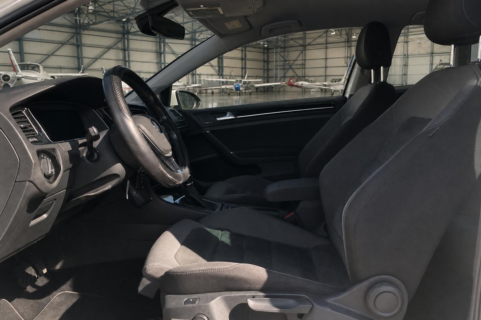 Volkswagen Golf Innenraum mit schwarzen Sportsitzen und Lenkrad in Hangar-Atmosphäre