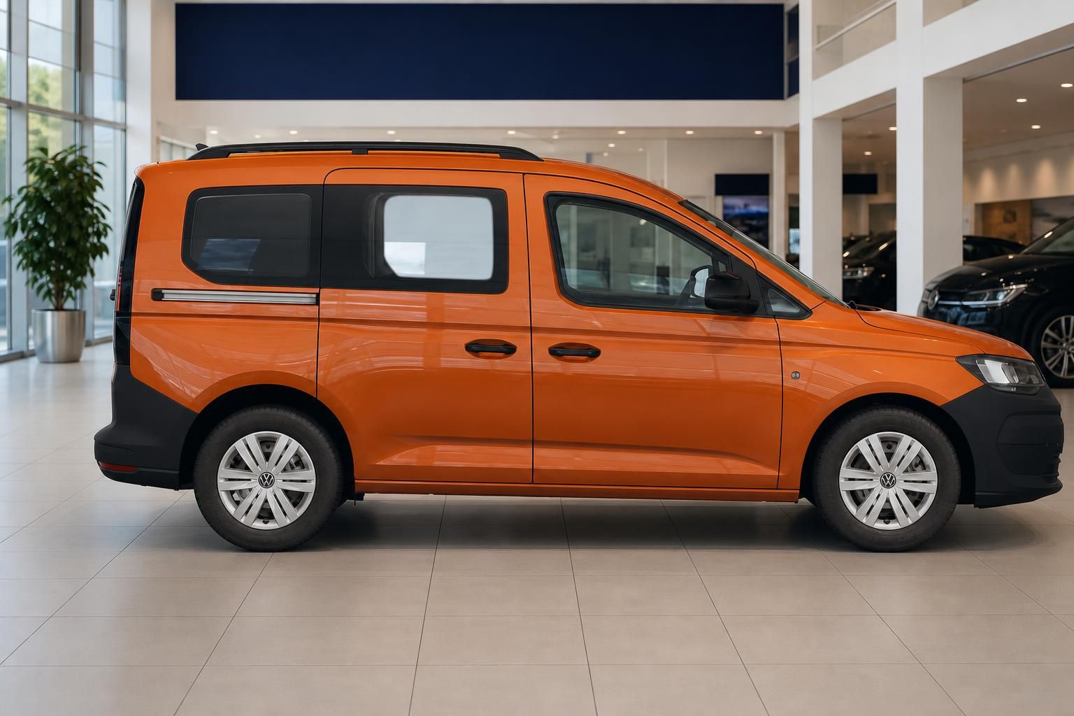 VW Caddy orange in Seitenansicht im Autohaus-Showroom