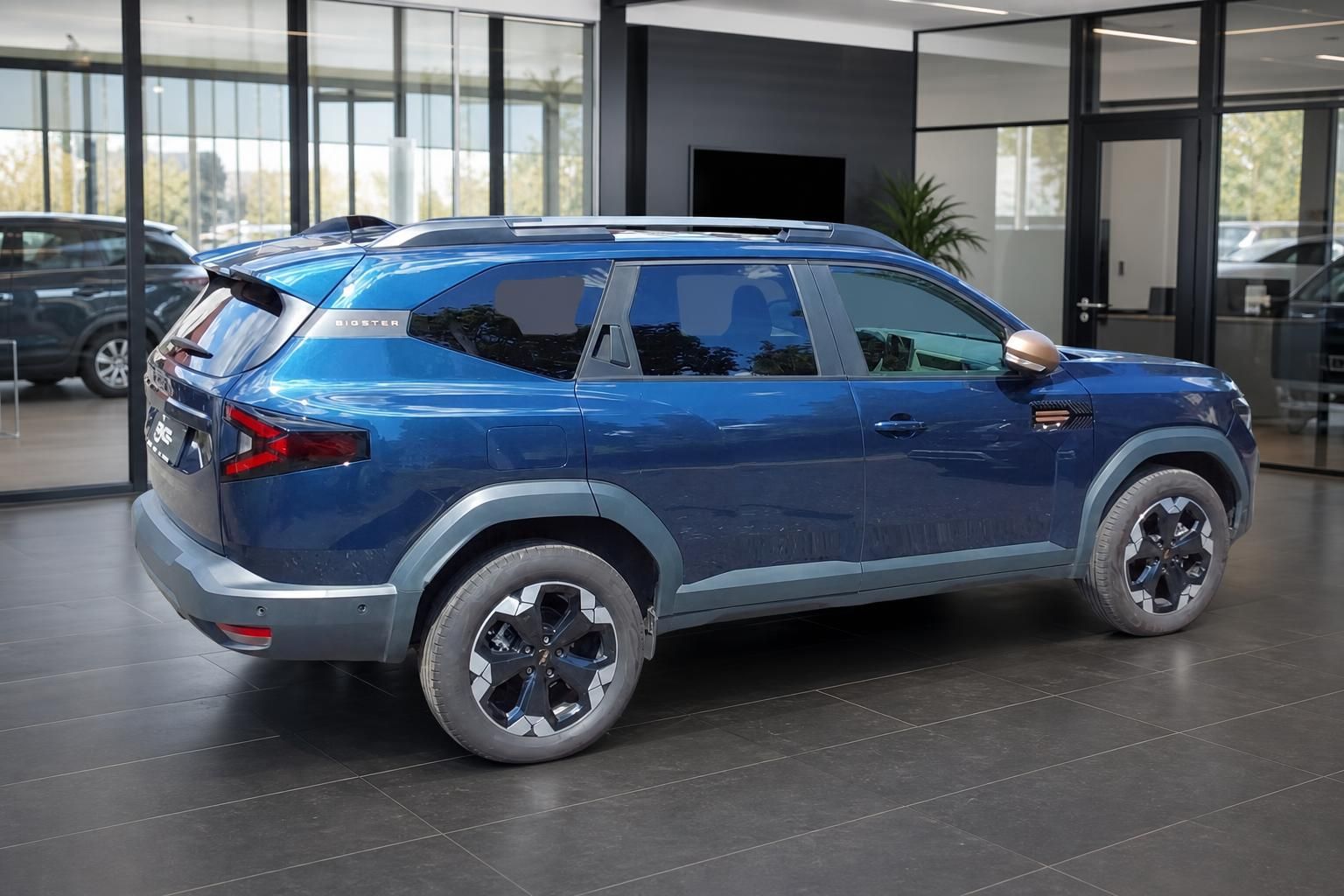 Dacia Bigster blau Heckansicht schräg im Showroom – SUV mit Dachspoiler und Chromfelgen