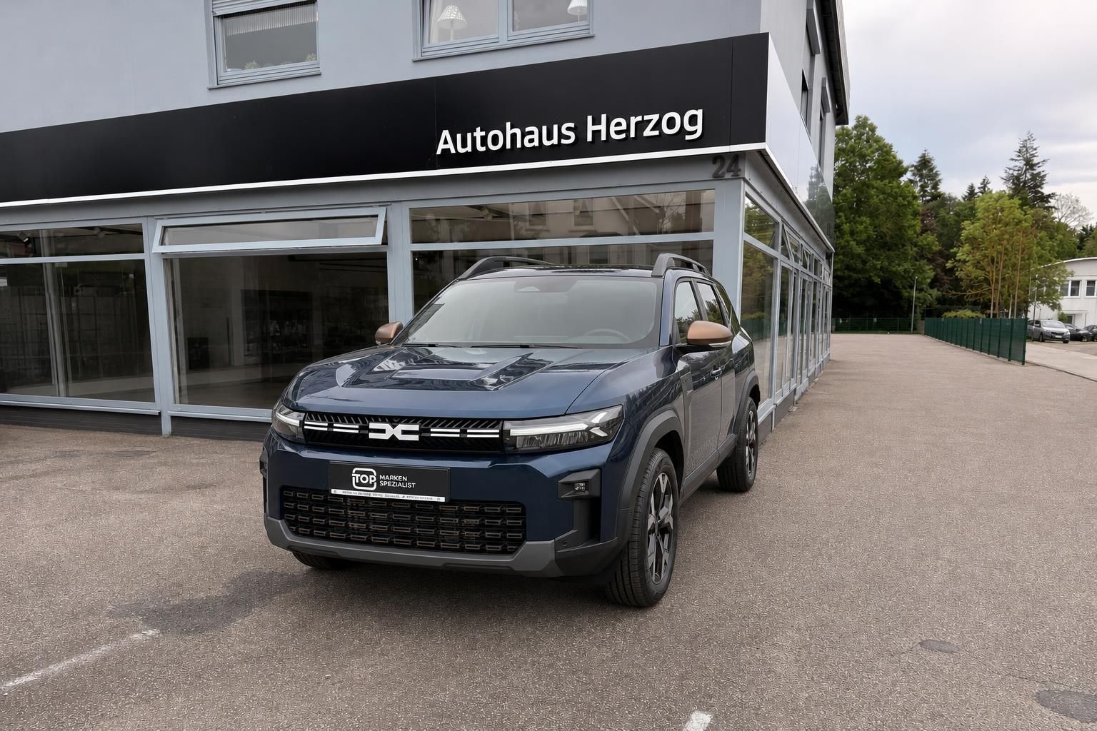 Dacia Jogger blau Frontansicht mit TOP Marken Spezialist Kennzeichenhalter vor Autohaus Herzog
