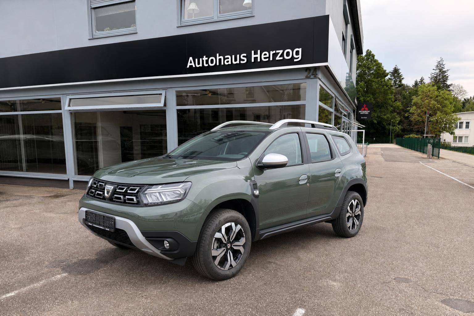 Dacia Duster SUV in Khaki-Grün vor Autohaus Herzog - Seitenansicht mit Alufelgen