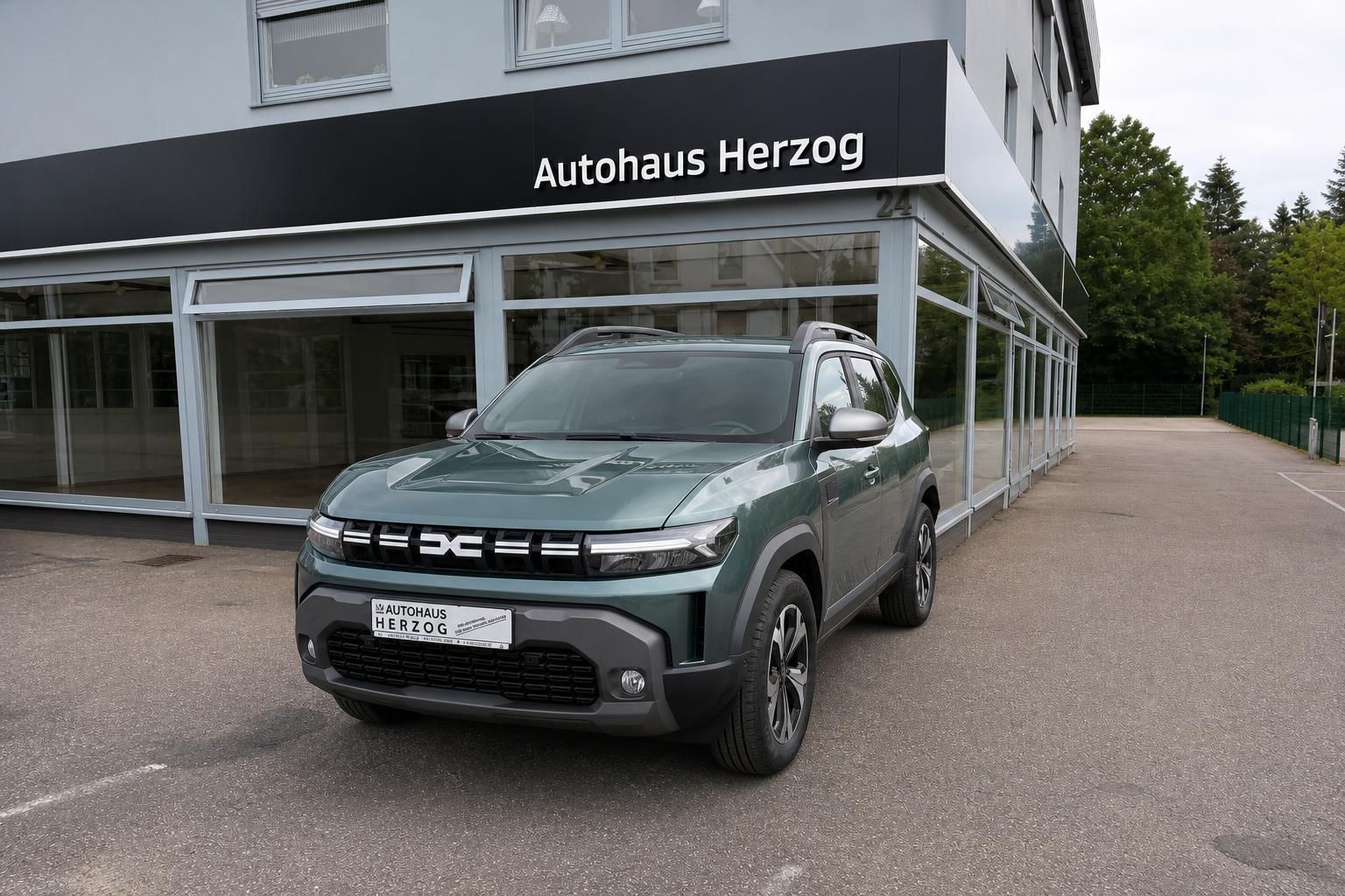 Grauer SUV Dacia Schrägansicht vorne - Fahrzeug vor Autohaus Herzog Showroom