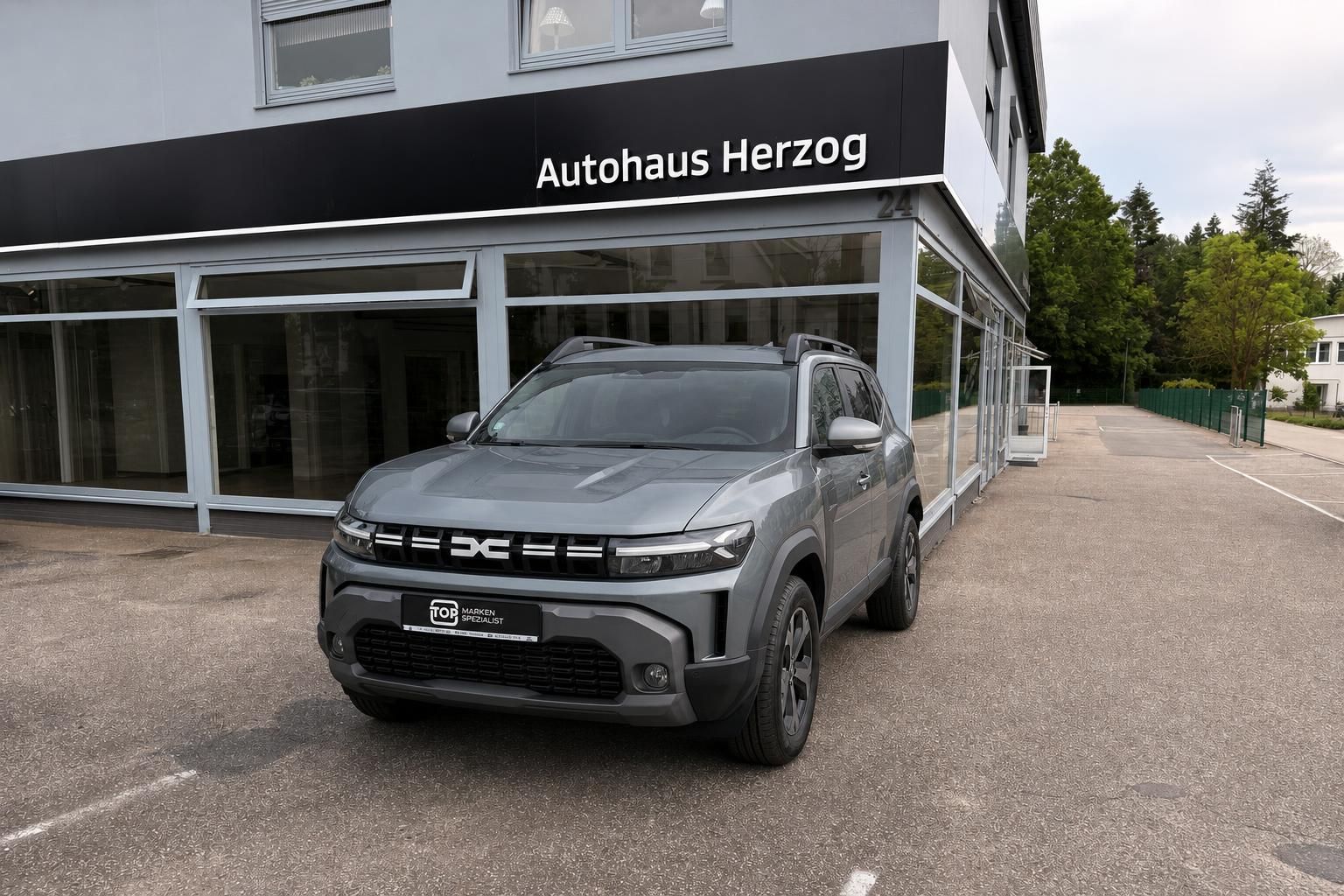 Dacia SUV grau Frontansicht mit Dachreling vor Showroom