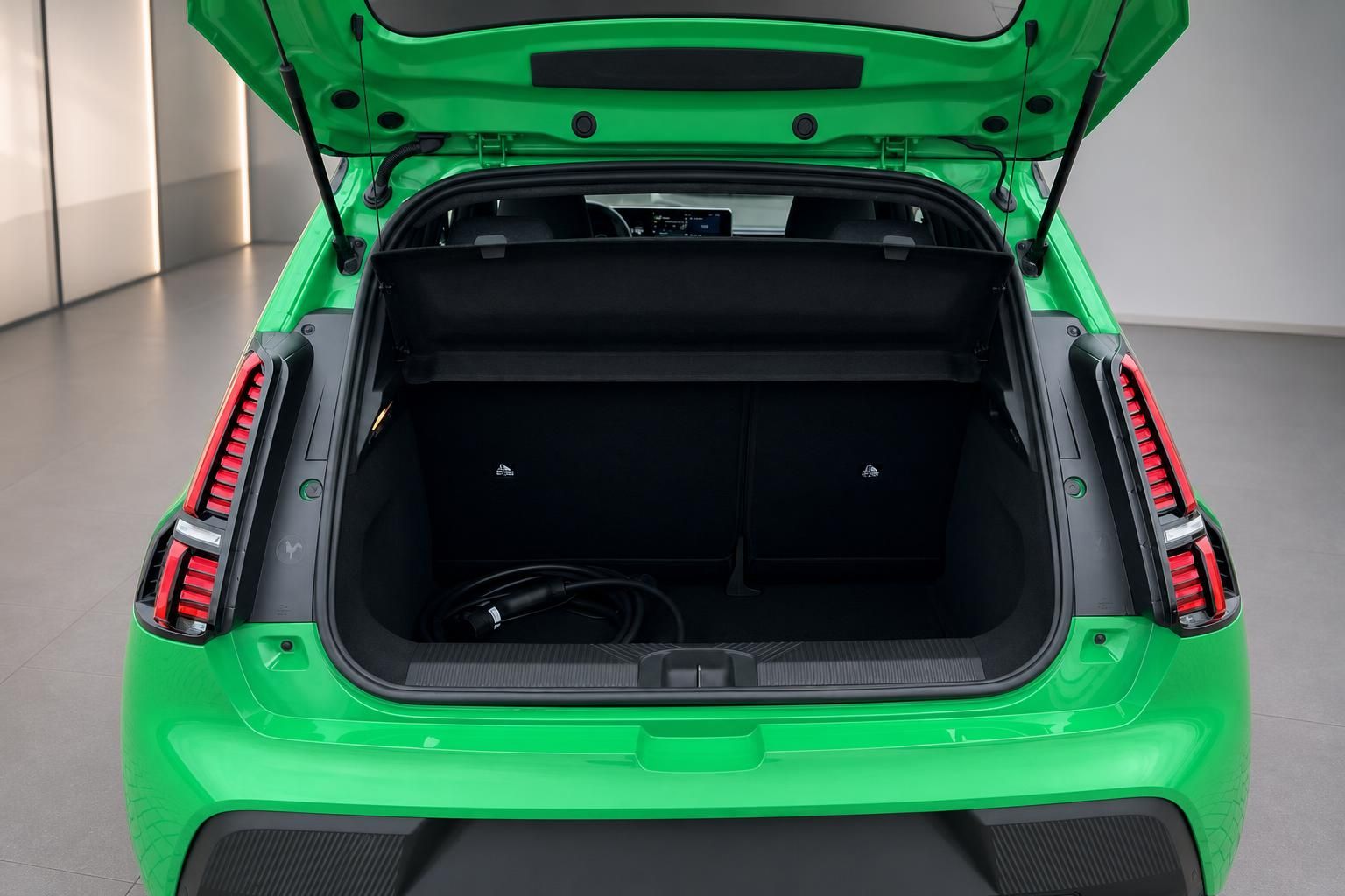 Geöffneter Kofferraum eines grünen Elektroautos mit Ladekabel und umklappbaren Rücksitzen