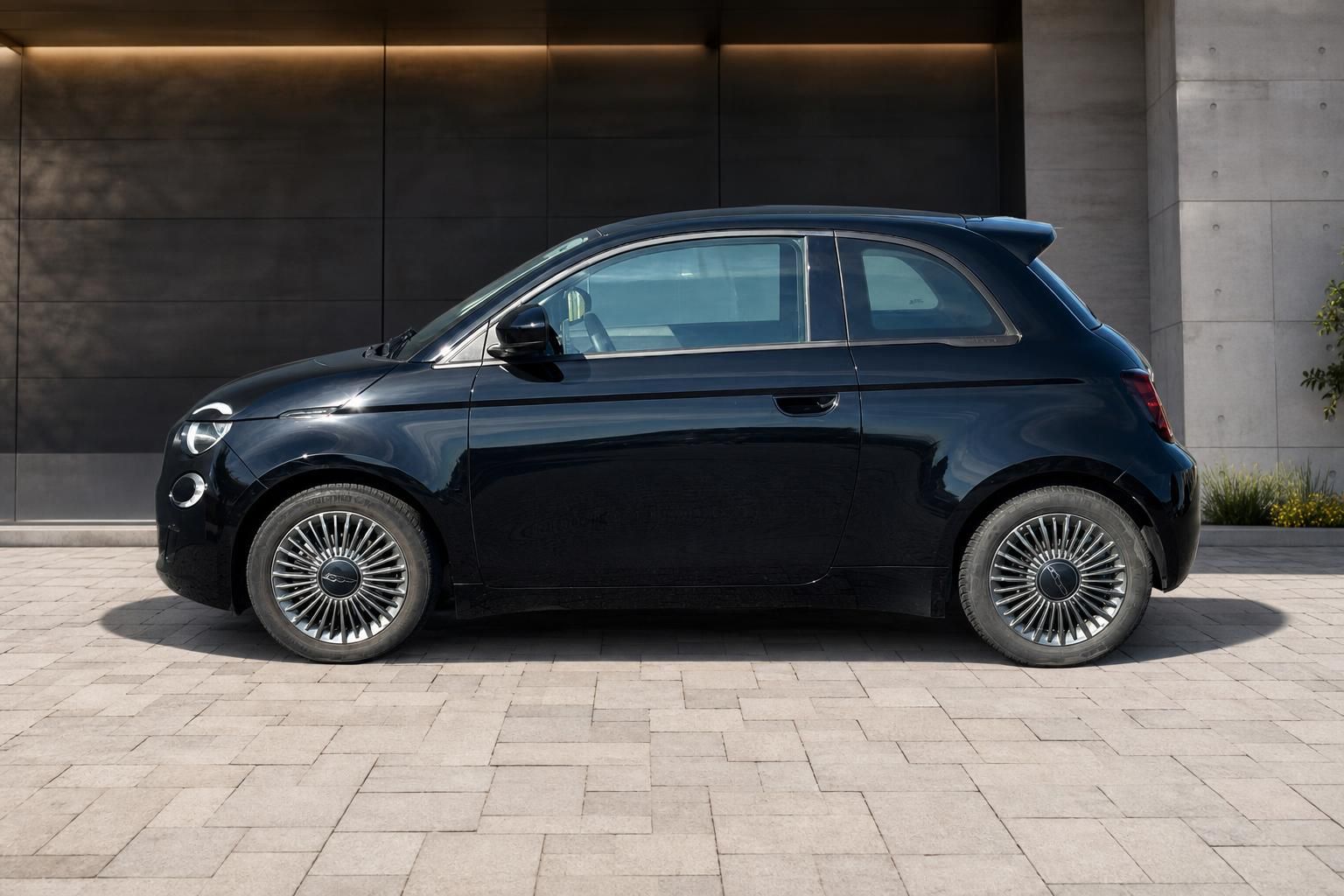 Fiat 500e Elektro schwarz Seitenansicht links auf Pflastersteinplatz