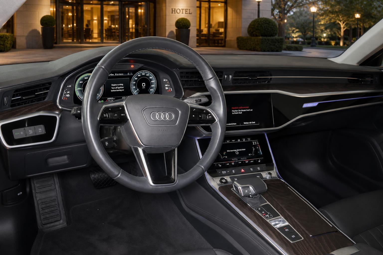 Audi Cockpit mit Lenkrad und Multimediadisplay vor Hoteleinfahrt bei Nacht