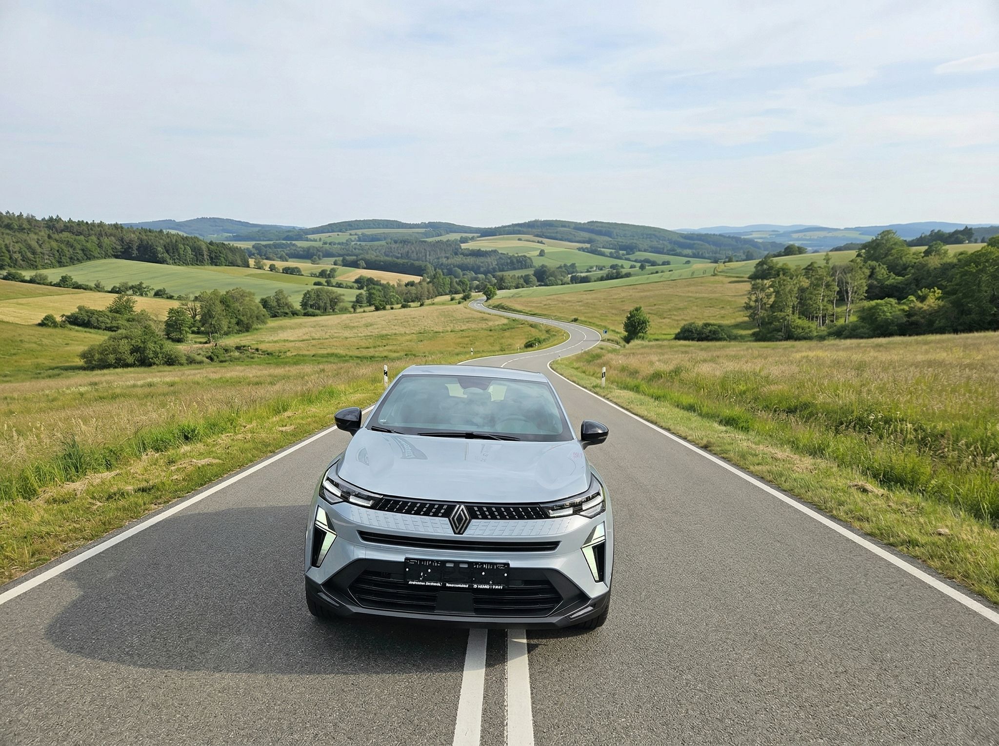 Renault Captur silber Elektro-SUV Frontansicht auf kurvenreicher Landstraße in hügeliger Landschaft