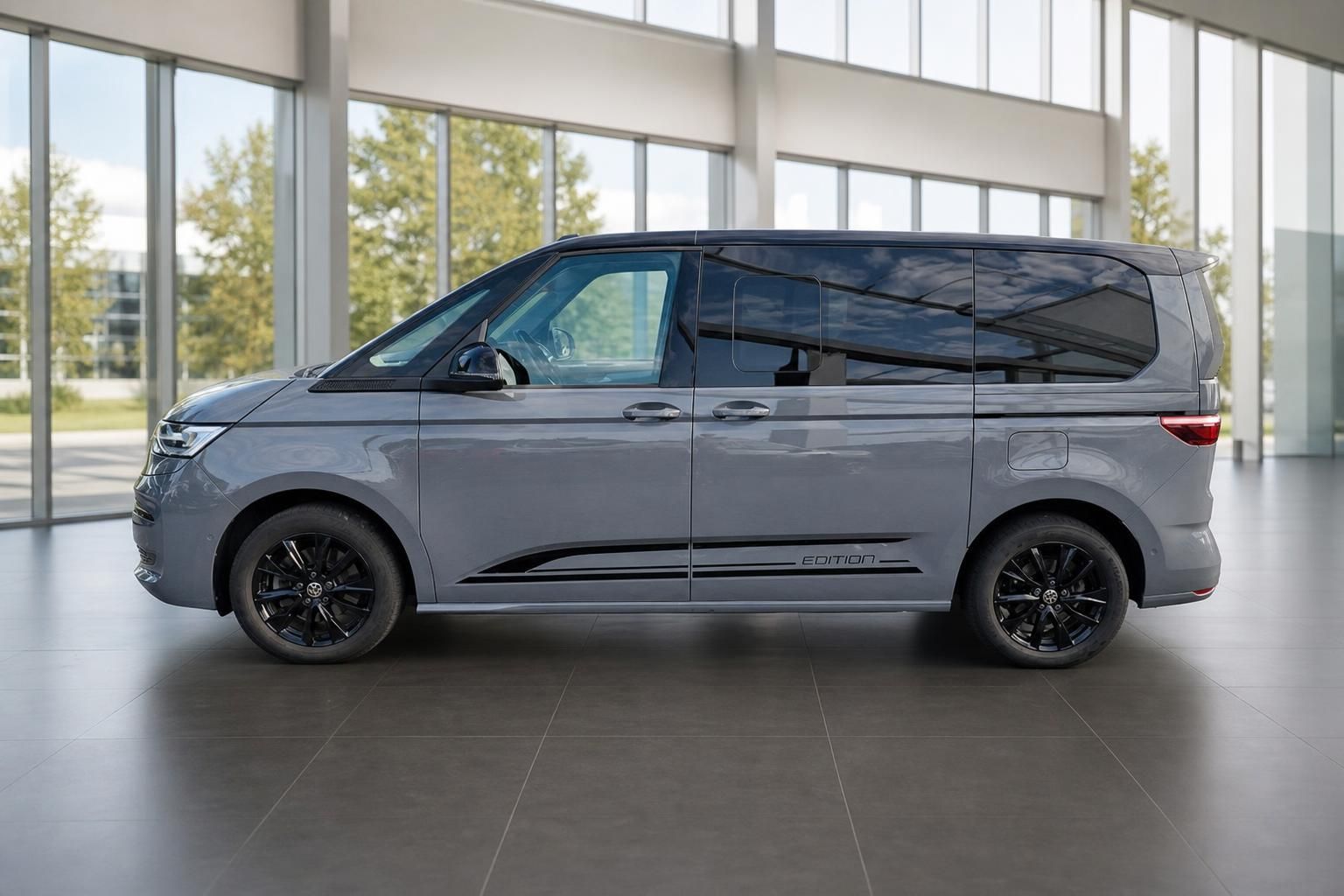 VW Multivan Edition in Grau, Seitenansicht in moderner Glashalle