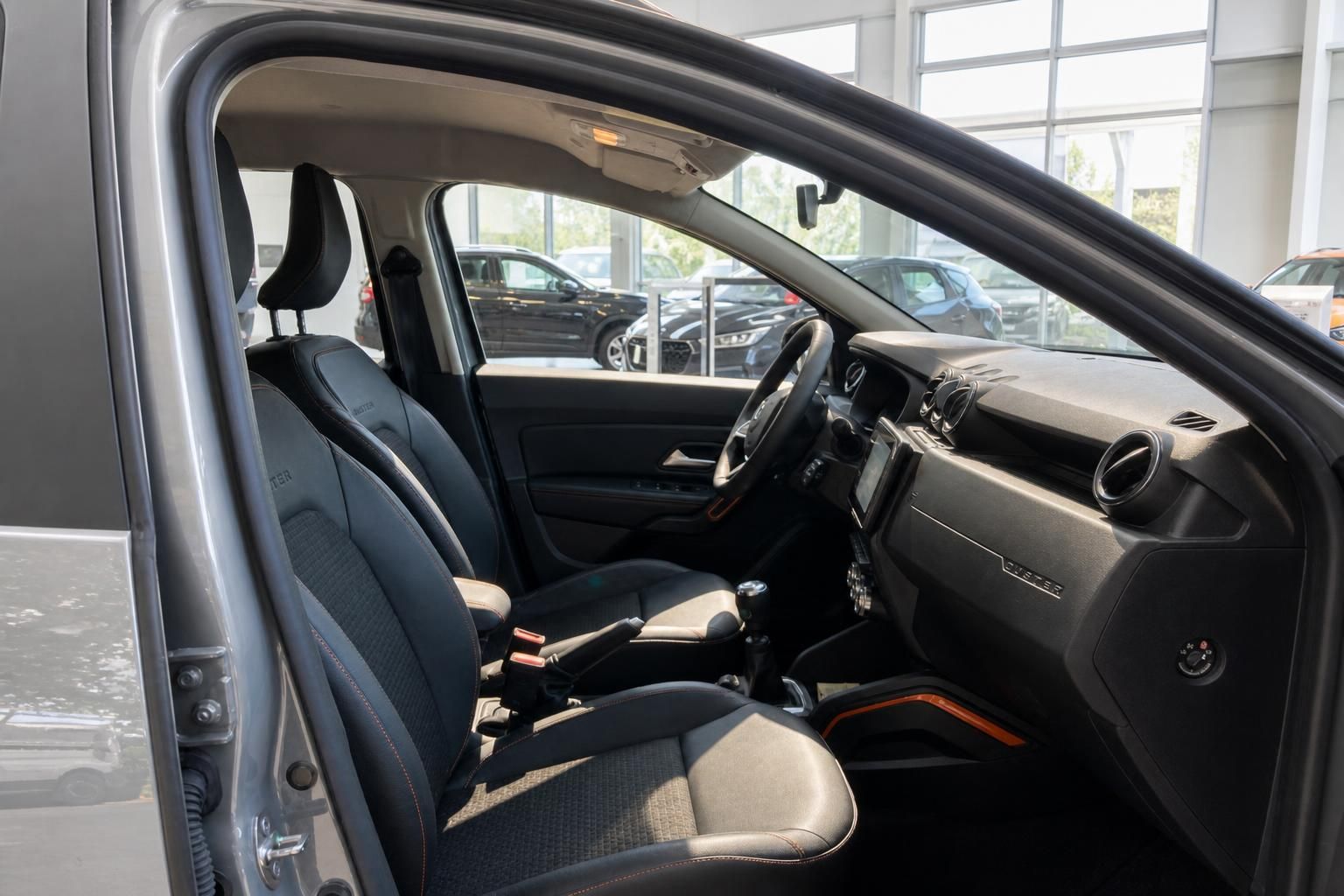 Dacia Duster Innenraum – Vordersitze mit schwarzem Stoff, Armaturenbrett und Mittelkonsole im Autohaus