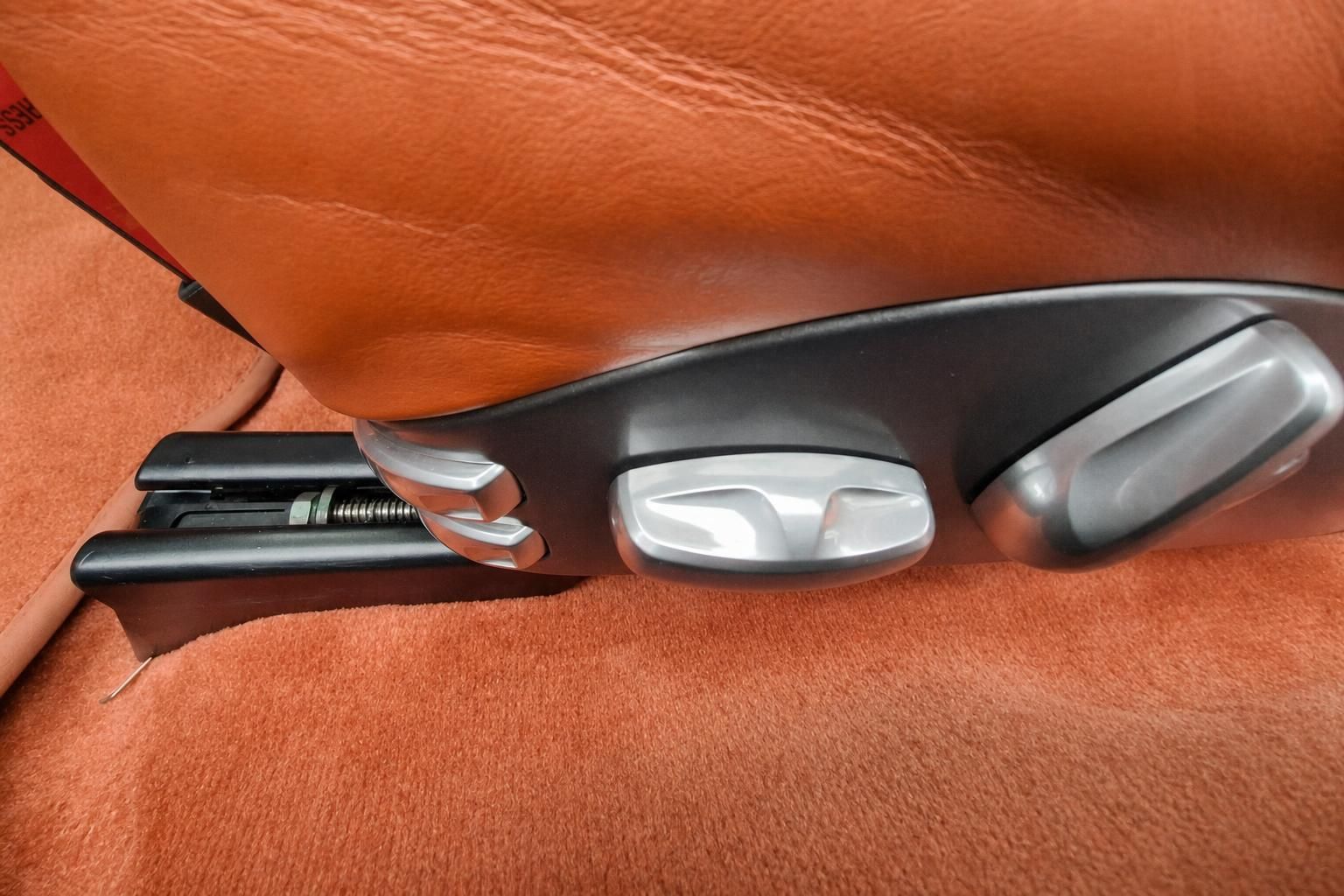 Detailaufnahme Porsche Sitzverstellung mit orangefarbenem Leder und Chromakzenten