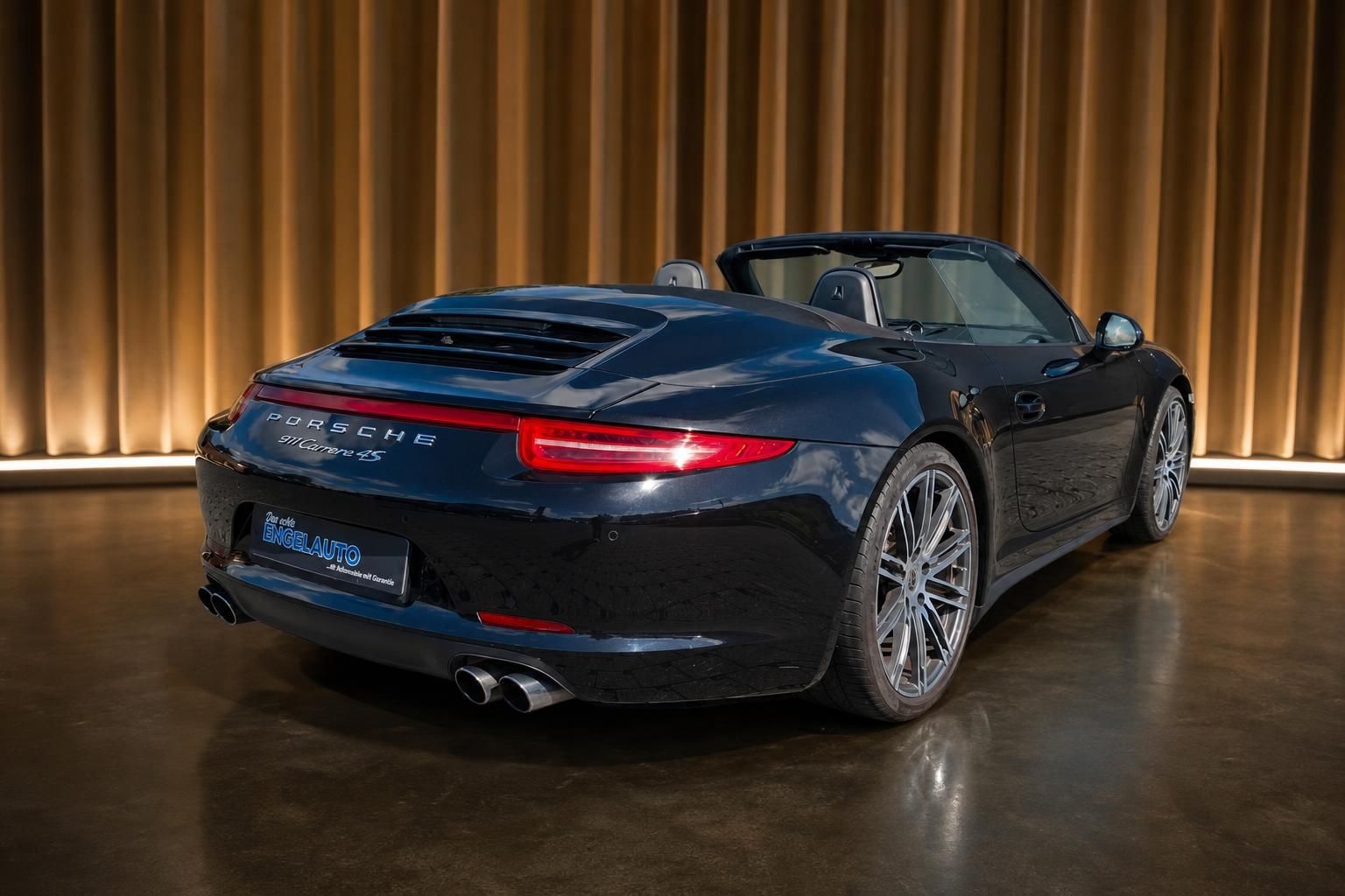 Porsche 911 Carrera 4S Cabrio in dunkelblau, seitliche Heckansicht mit Holzwand im Hintergrund