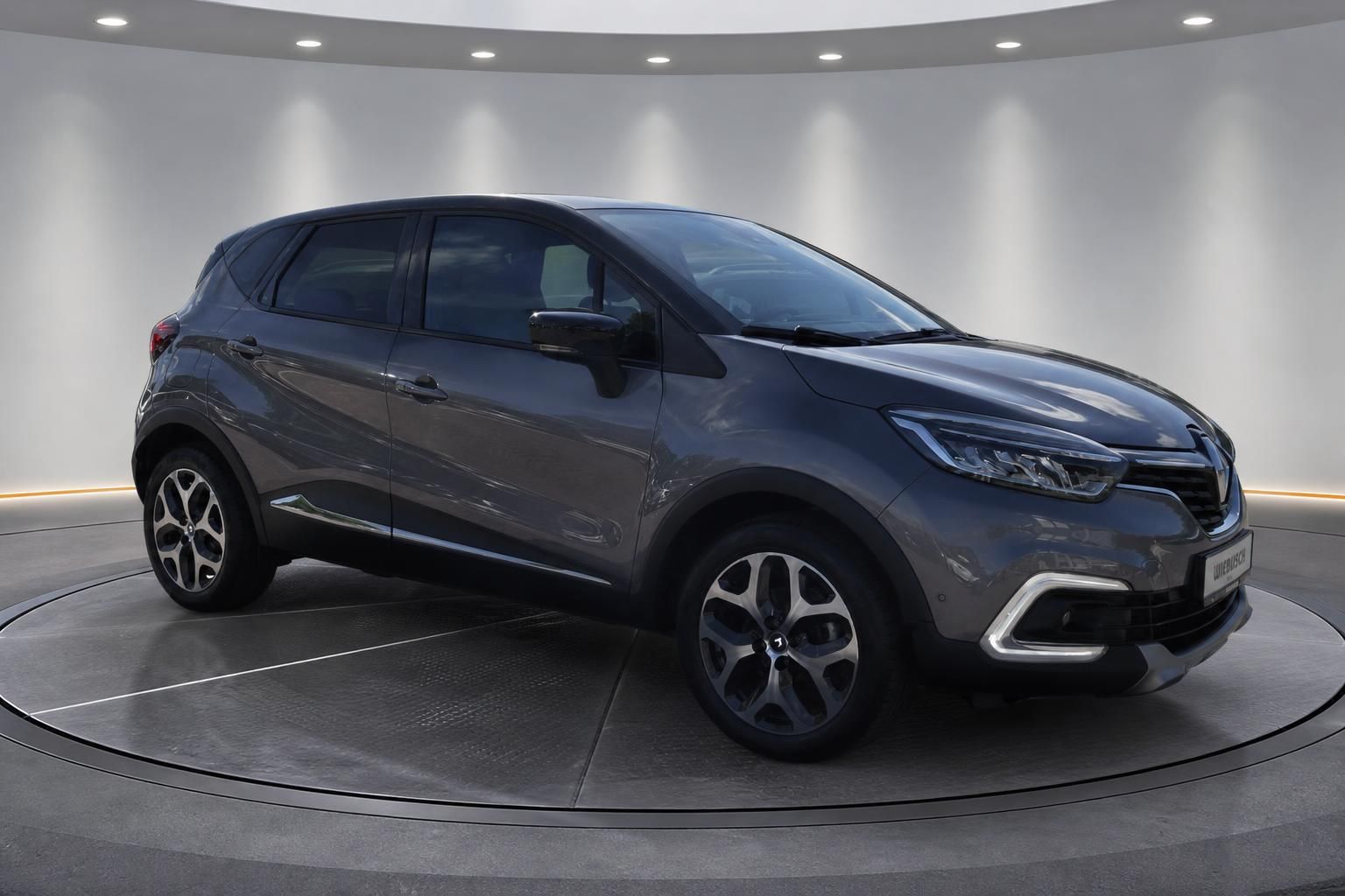 Renault Captur grau Schrägansicht hinten links auf Drehteller im Ausstellungsraum