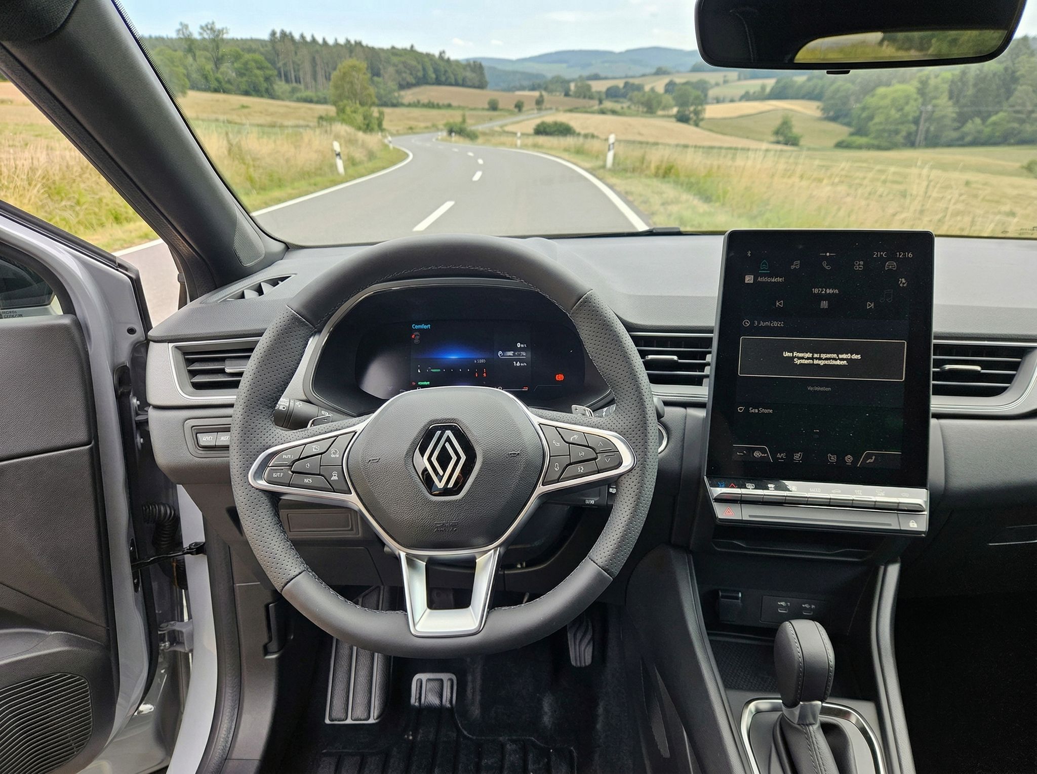 Renault Captur Innenraum mit Lenkrad, digitalem Cockpit und Touchscreen-Display bei Landstraßenblick