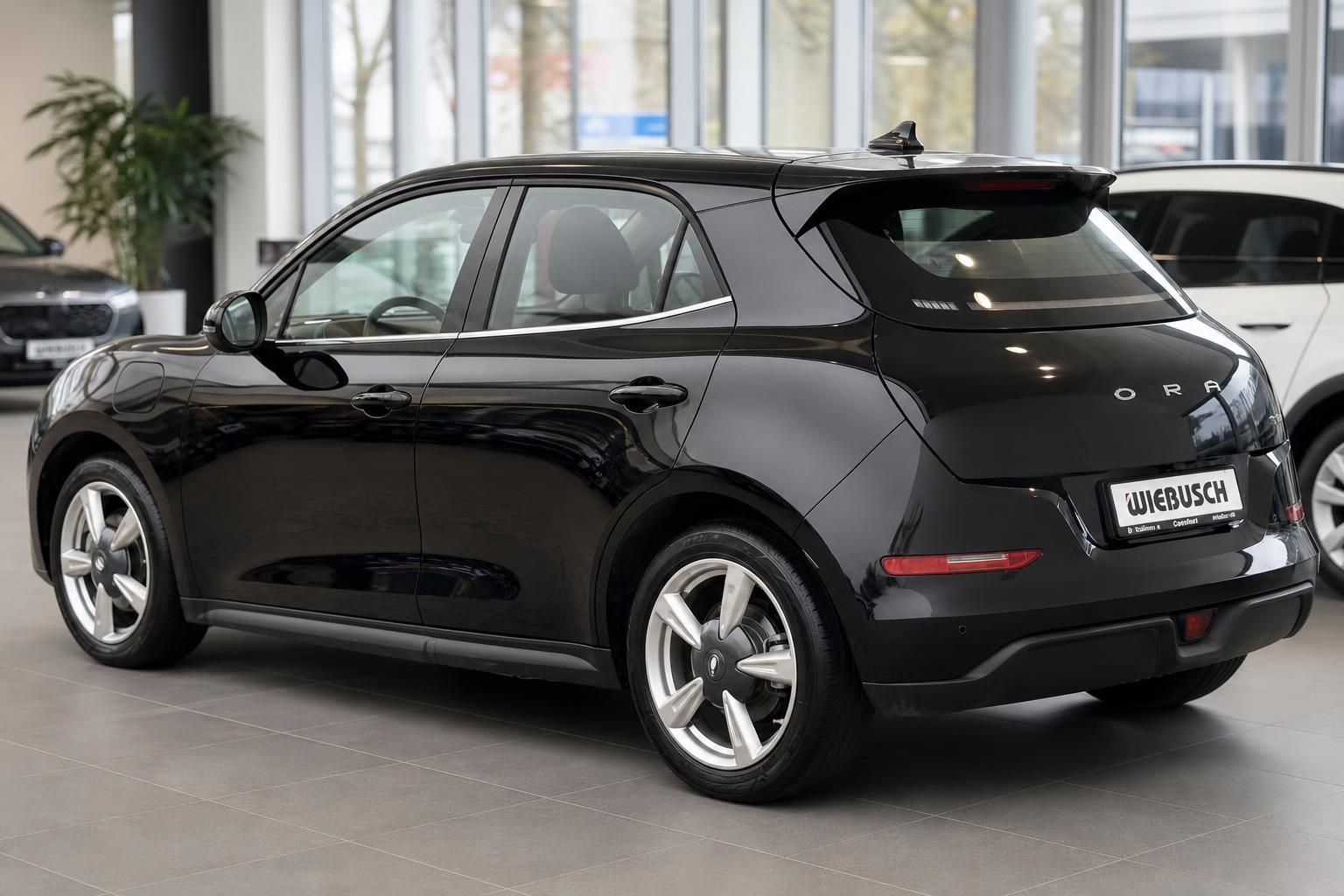 Schwarzer Elektro-Kleinwagen im Autohaus-Showroom, Heckansicht mit modernem LED-Rücklicht und Spoiler