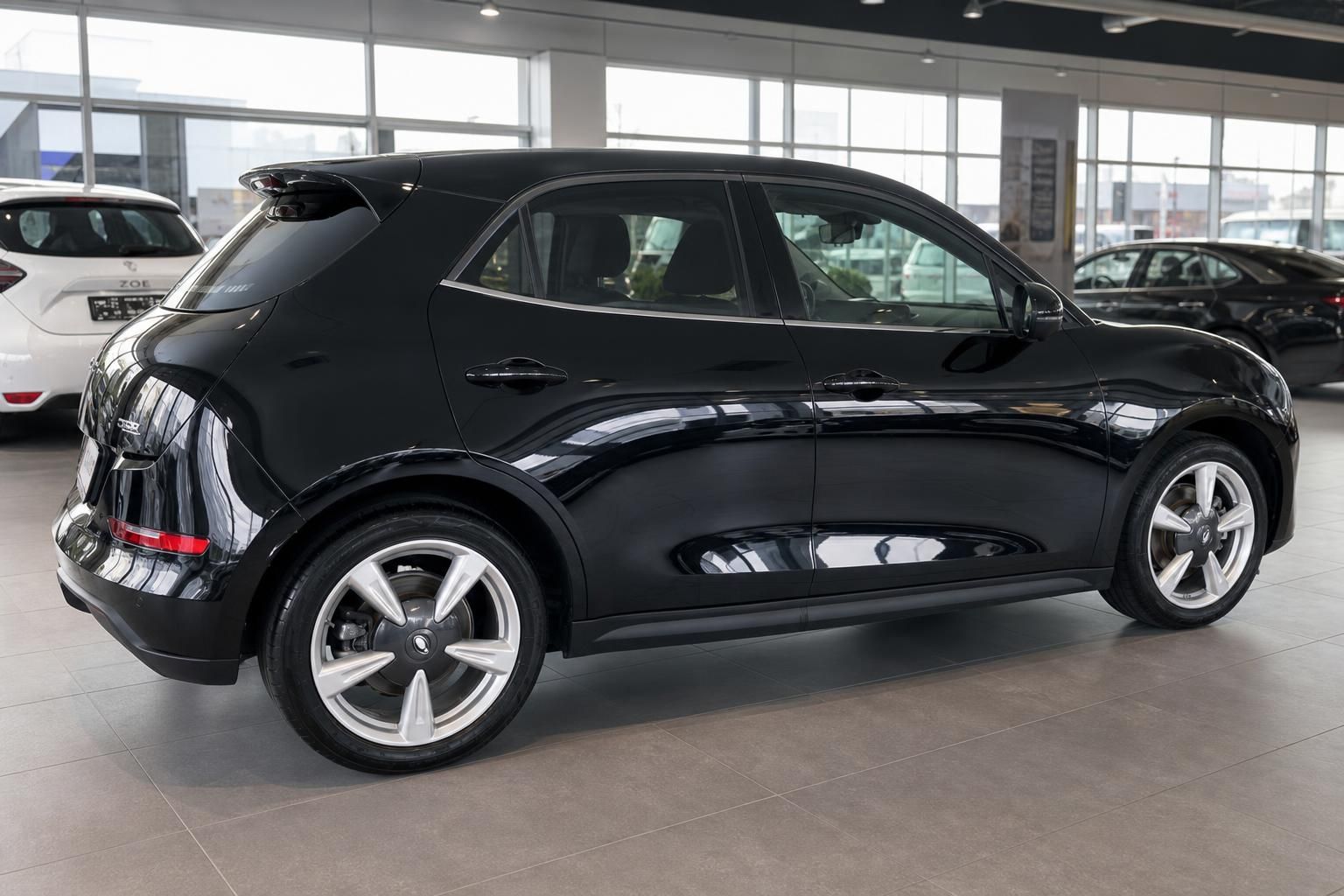 Schwarzer Elektro-Kleinwagen im Autohaus, seitliche Heckansicht mit sportlichen Felgen und elegantem Design