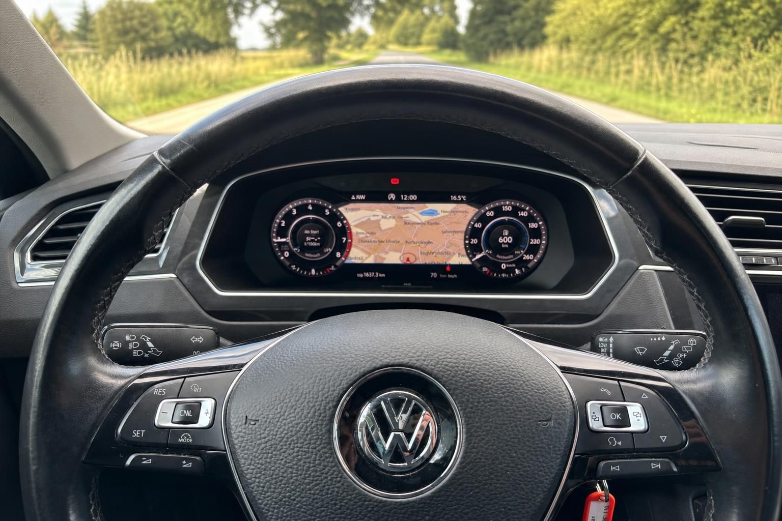 VW Lenkrad mit digitalem Kombiinstrument und Navigationskarte auf Landstrasse
