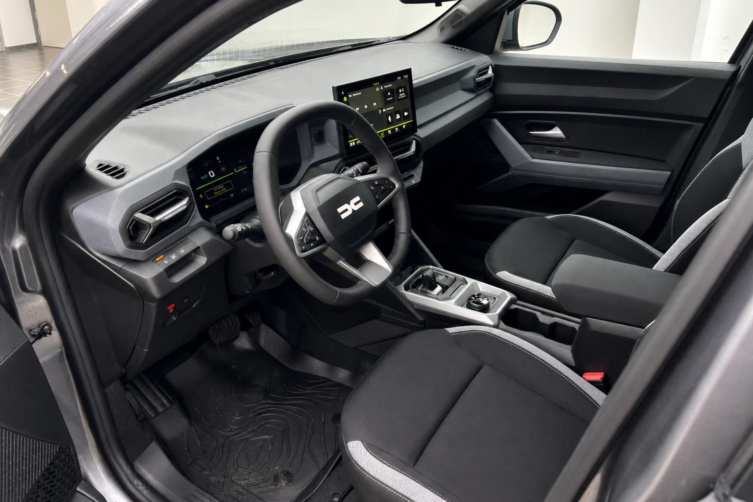 Dacia Innenraum Fahrerseite mit Lenkrad, Mittelkonsole und schwarzen Stoffsitzen