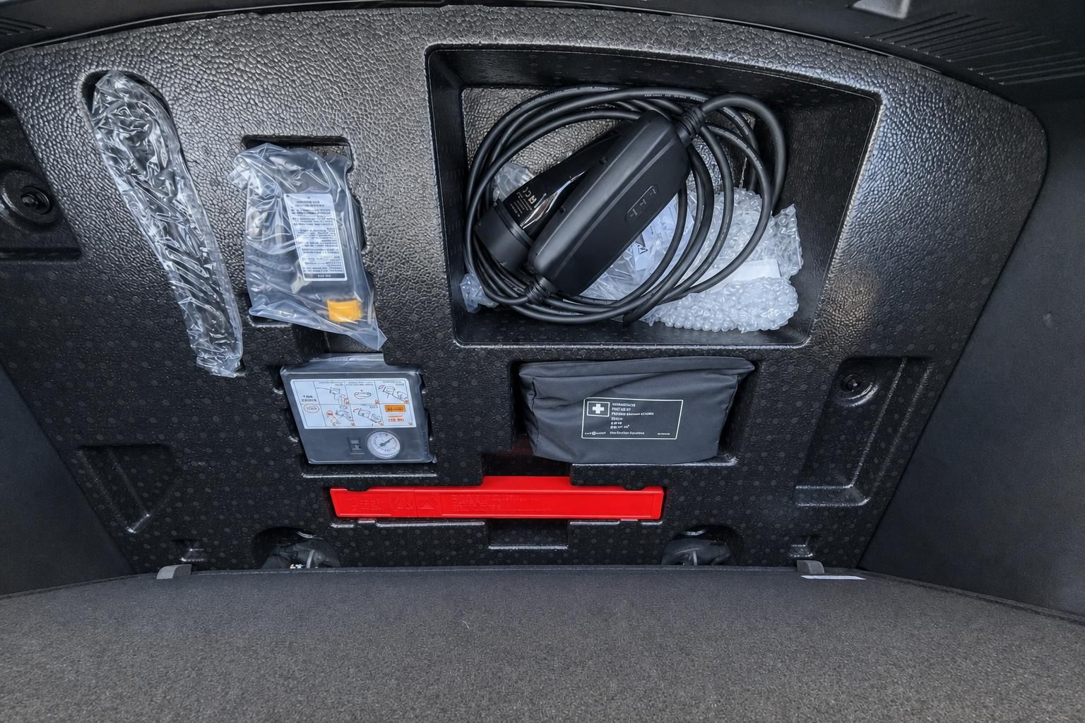 Kofferraum mit Ladekabel, Kompressor, Erste-Hilfe-Set und weiterem Zubehör im offenen Staufach
