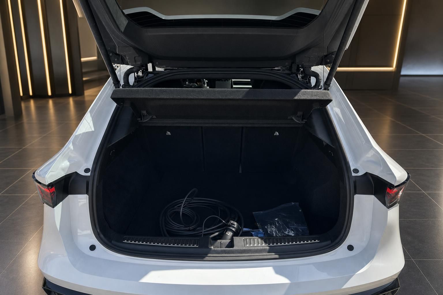 Kofferraum eines weißen Elektroautos mit Ladekabel und geöffneter Heckklappe
