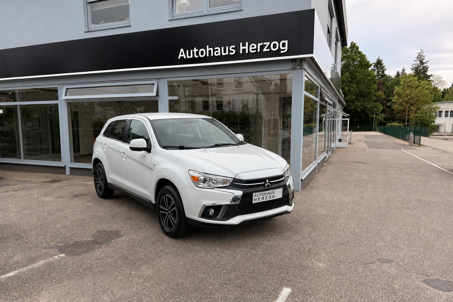 Weißer Mitsubishi SUV vor Autohaus Herzog - Seitenansicht des geparkten Fahrzeugs