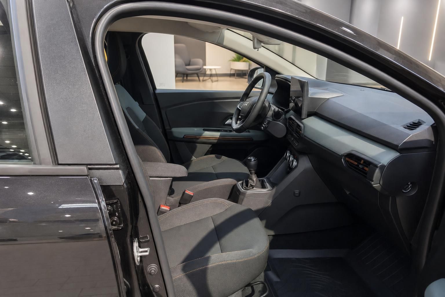 Dacia Innenraum Fahrerseite geöffnete Tür mit Vordersitzen, Lenkrad und Mittelkonsole im Autohaus