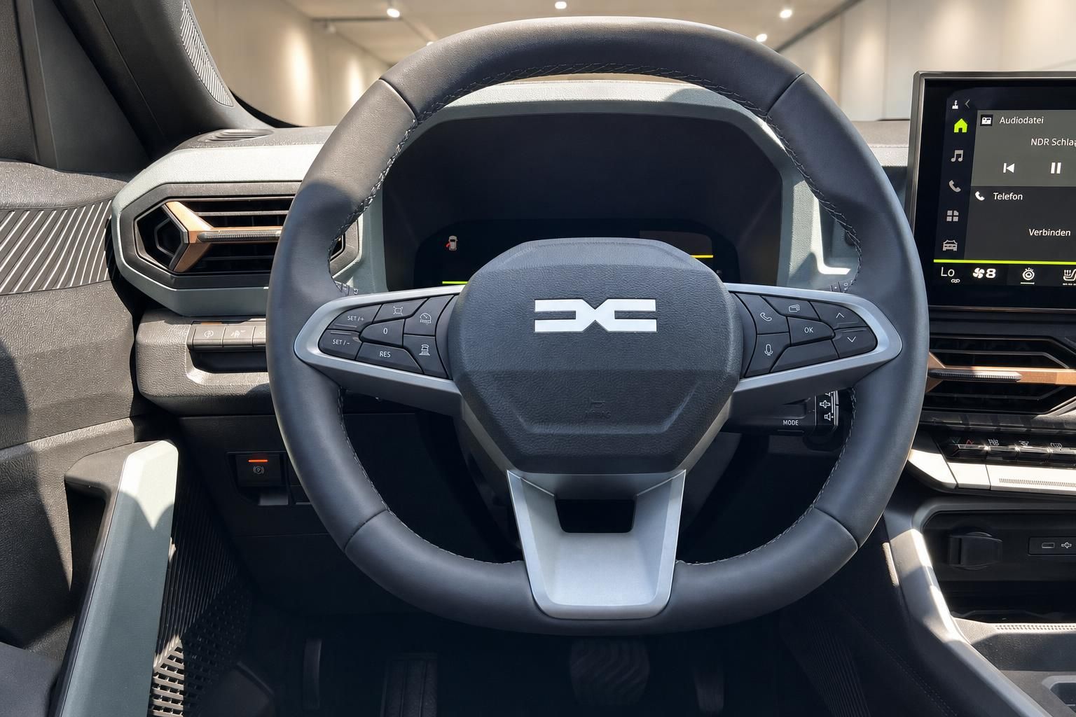 Dacia Lenkrad mit Logo und digitalem Cockpit sowie Touchscreen-Infotainment im Hintergrund
