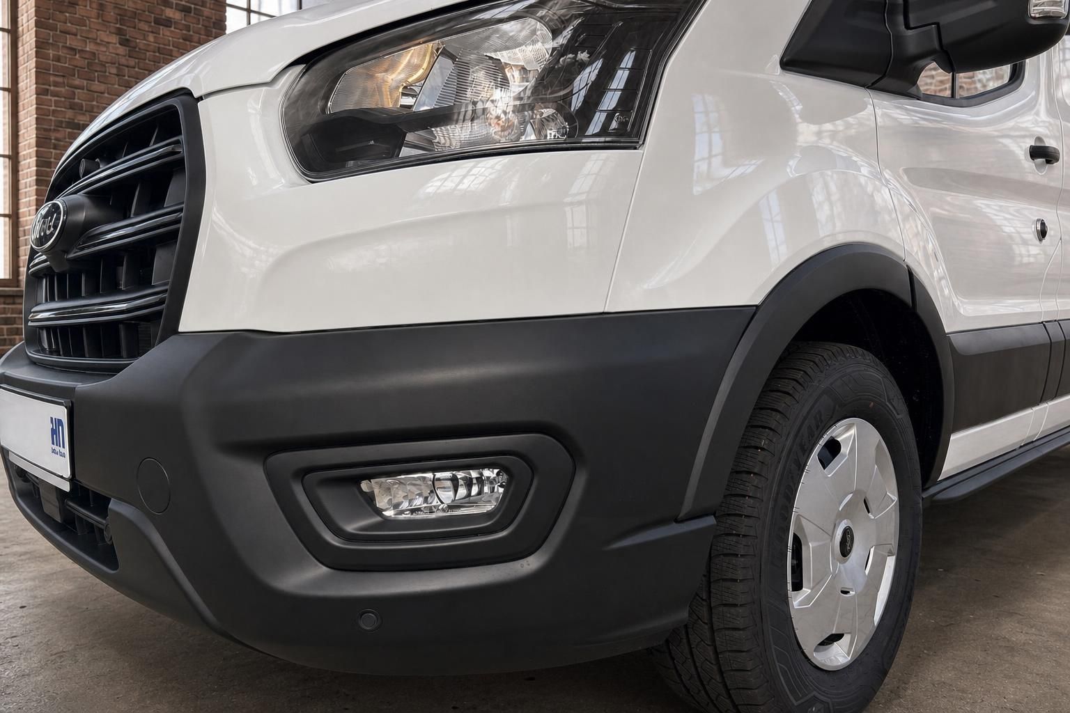 Ford Transit Nahaufnahme Front mit Scheinwerfer, schwarzem Stoßfänger und Vorderrad in Weiß