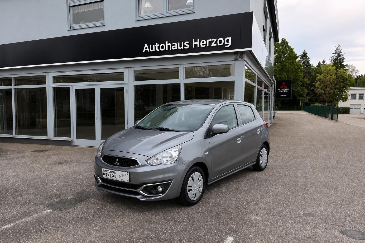 Grauer Mitsubishi Space Star Frontansicht vor Autohaus Herzog Glasfront