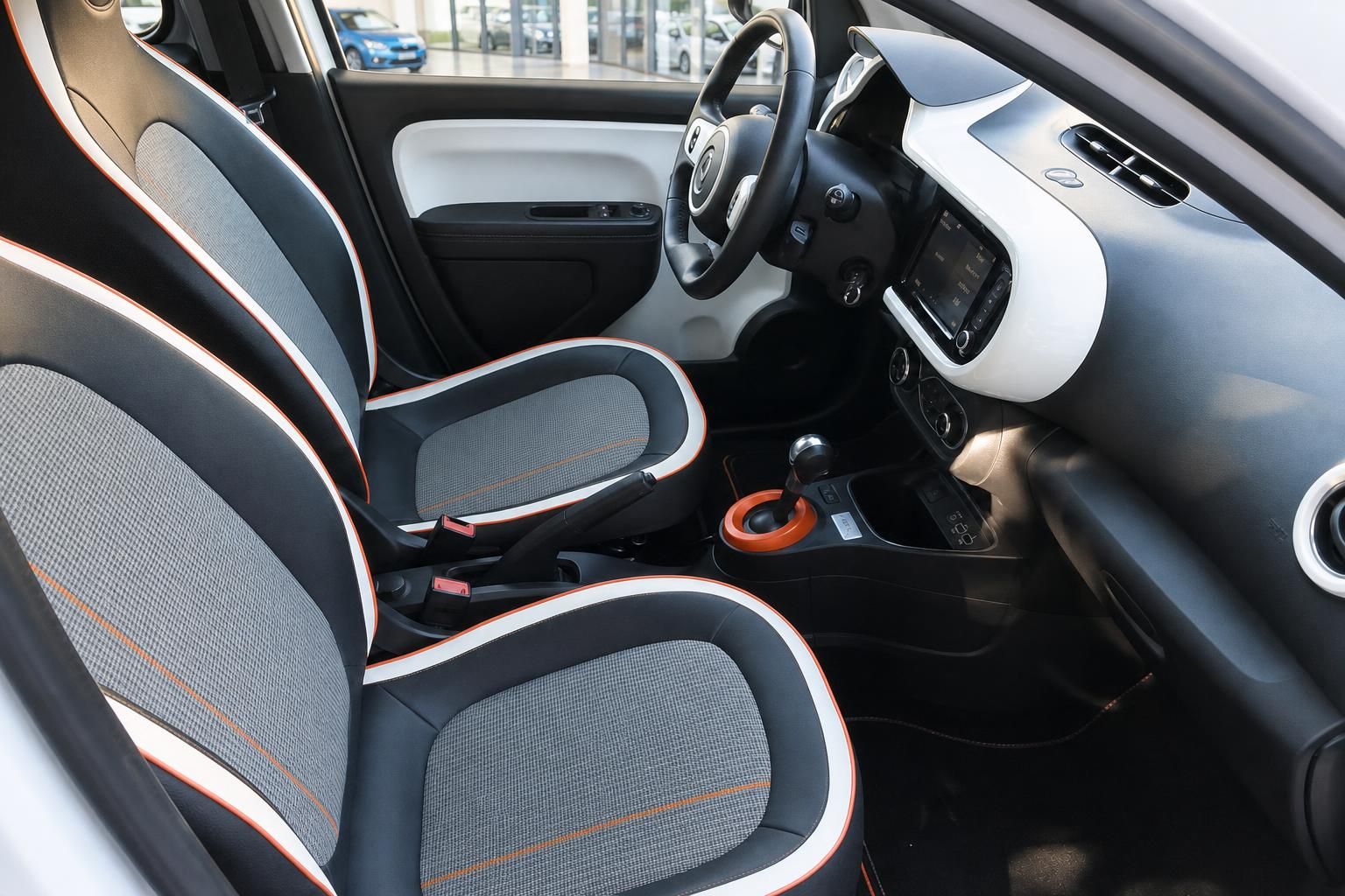 Fahrzeuginnenraum mit grauen Sitzen und orangen Ziernähten, Lenkrad und Armaturenbrett sichtbar
