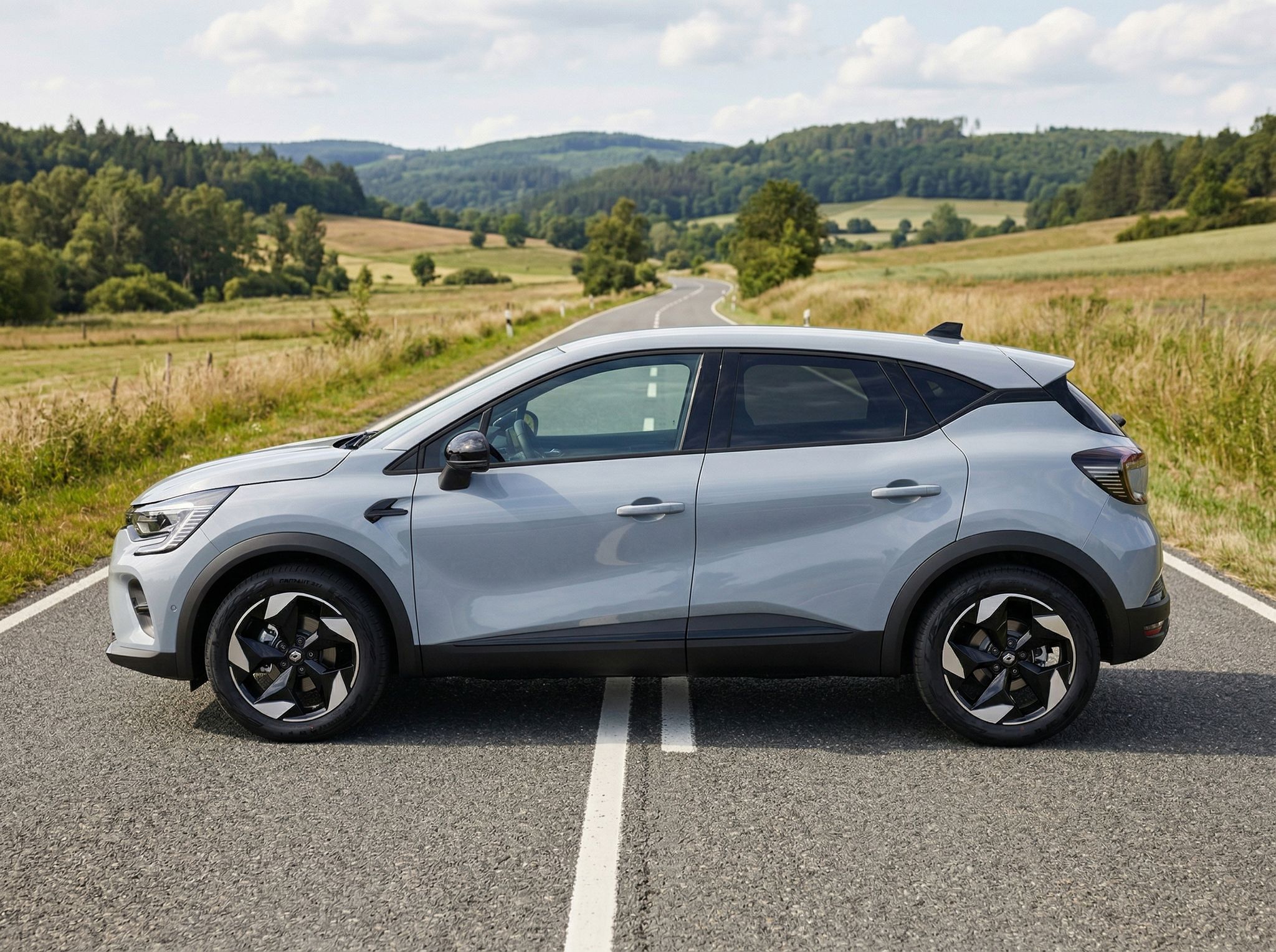 Renault Captur SUV silber seitlich auf Landstraße mit Hügeln im Hintergrund