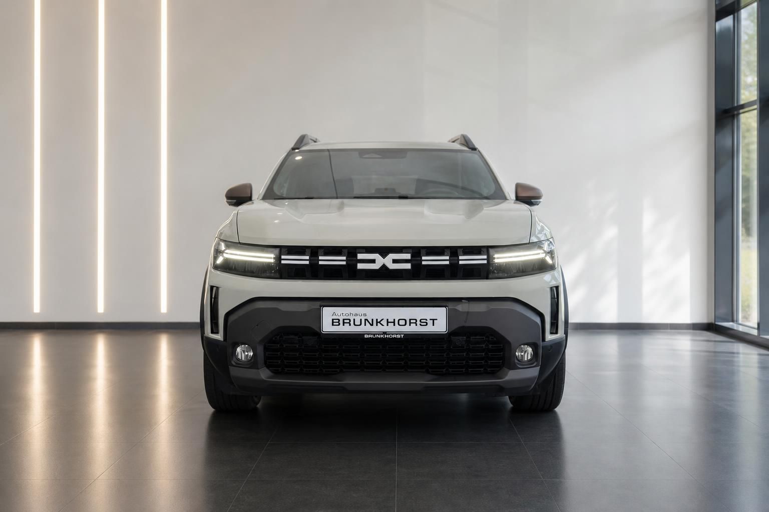 Dacia Duster Frontansicht - weißer SUV mit schwarzen Akzenten und LED-Tagfahrlicht im Showroom