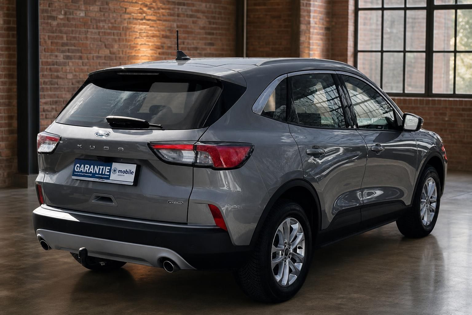 Ford Kuga Hybrid grau, Heckansicht seitlich in Loft-Ambiente