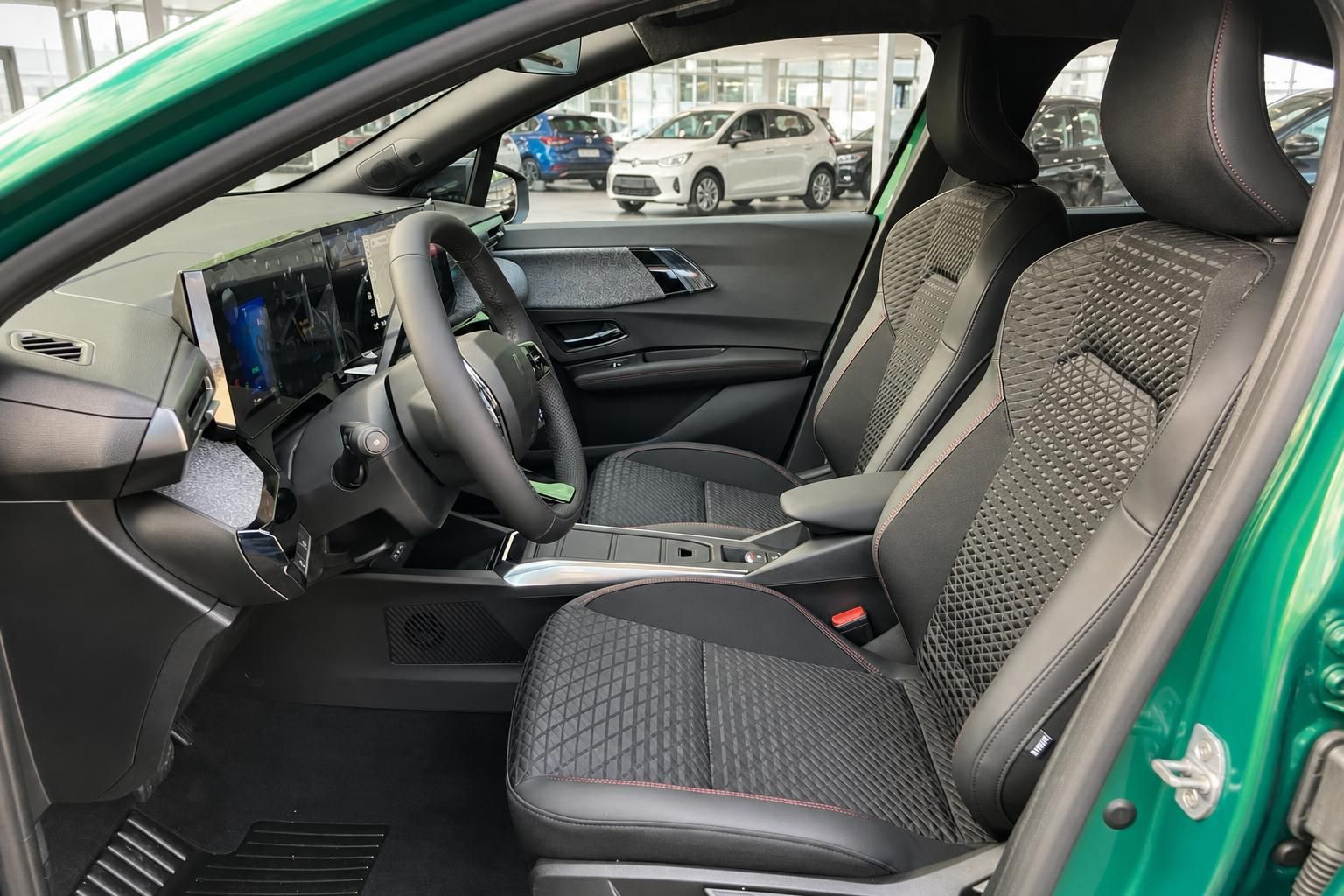 Innenraum grünes Auto – schwarze Sportsitze mit Rautenmuster, großes Touchscreen-Display und Lenkrad