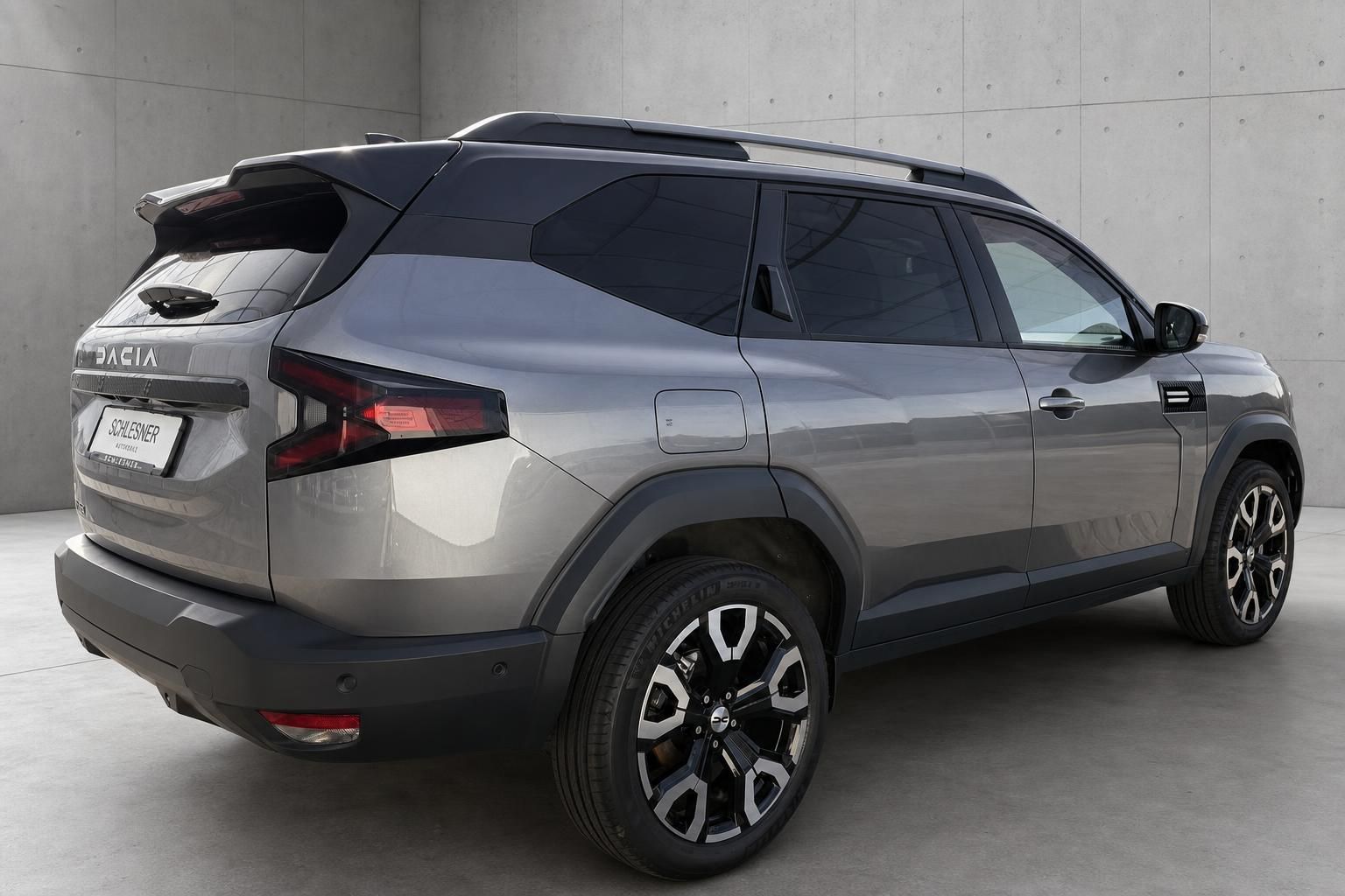 Dacia Bigster SUV in Grau, Heckansicht schraeg mit Dachreling