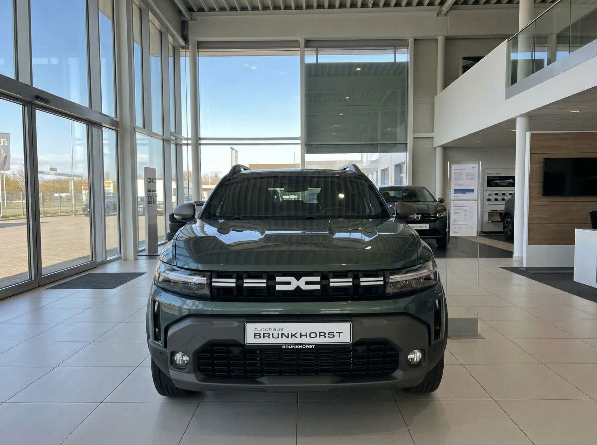 Dacia SUV grün metallic - Frontansicht im Autohaus mit Brunkhorst Kennzeichenhalter