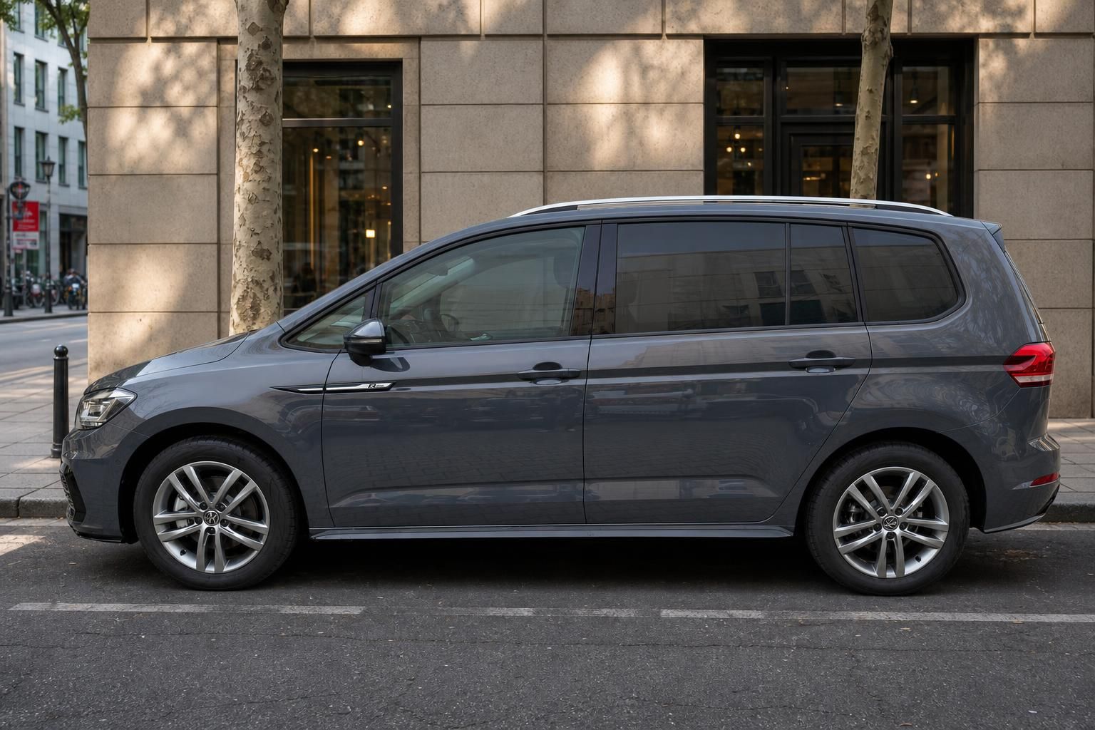 VW Touran grau metallic Seitenansicht, kompakter Van mit Alufelgen in urbaner Umgebung