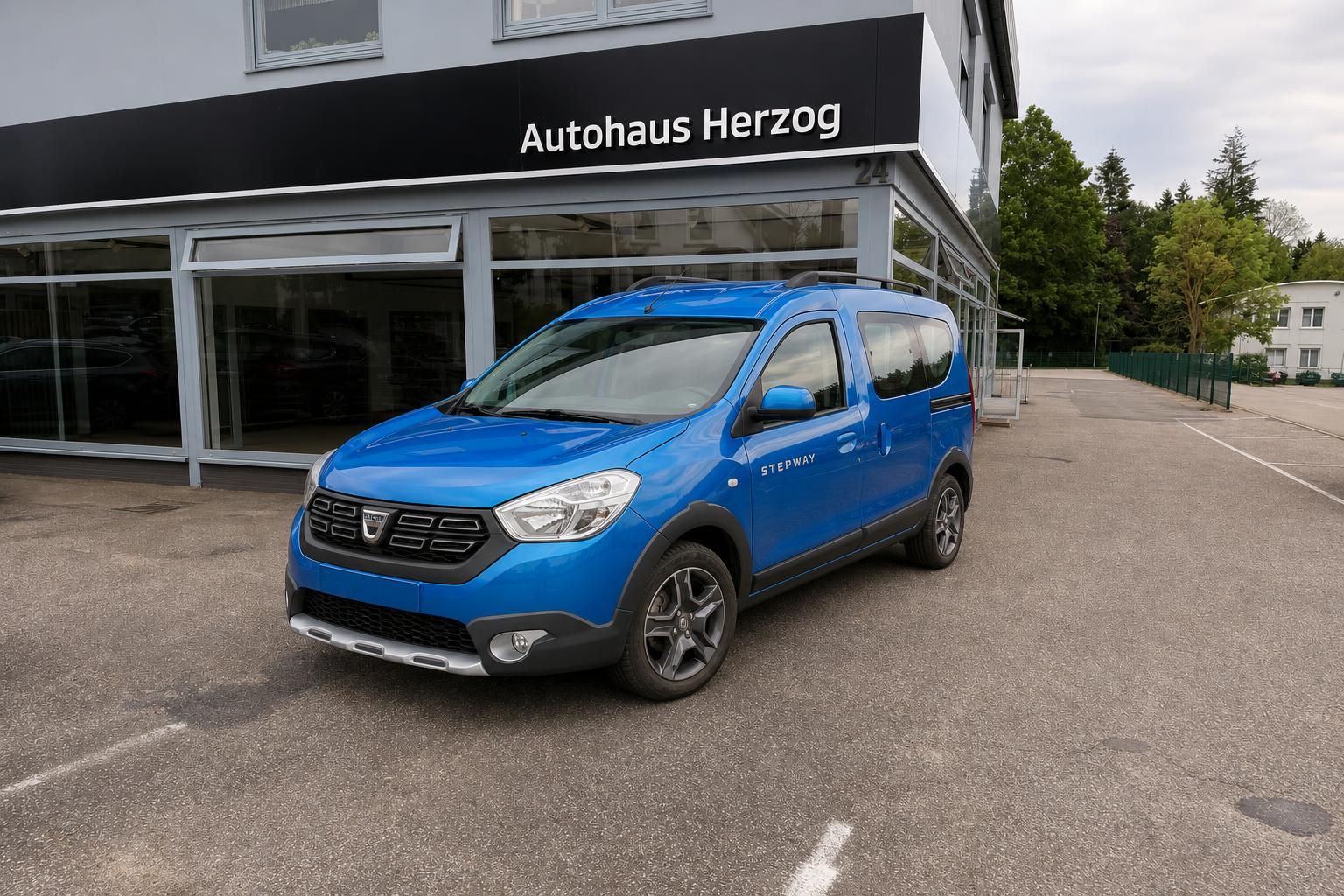 Blauer Dacia Stepway vor Autohaus Herzog - Seitenansicht des Kompakt-SUVs