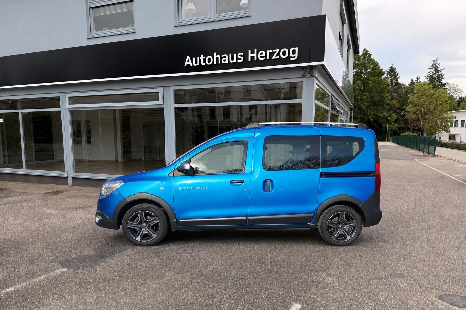 Blauer Dacia Dokker Stepway Van - Seitenansicht von links vor Autohaus Herzog