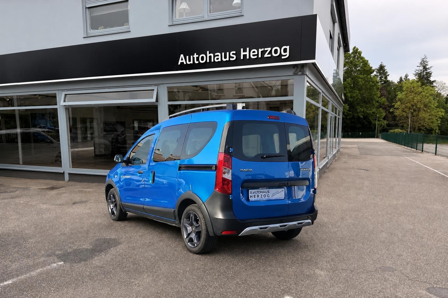 Blauer Dacia Dokker Stepway Van - Schrägansicht von hinten rechts vor Autohaus Herzog